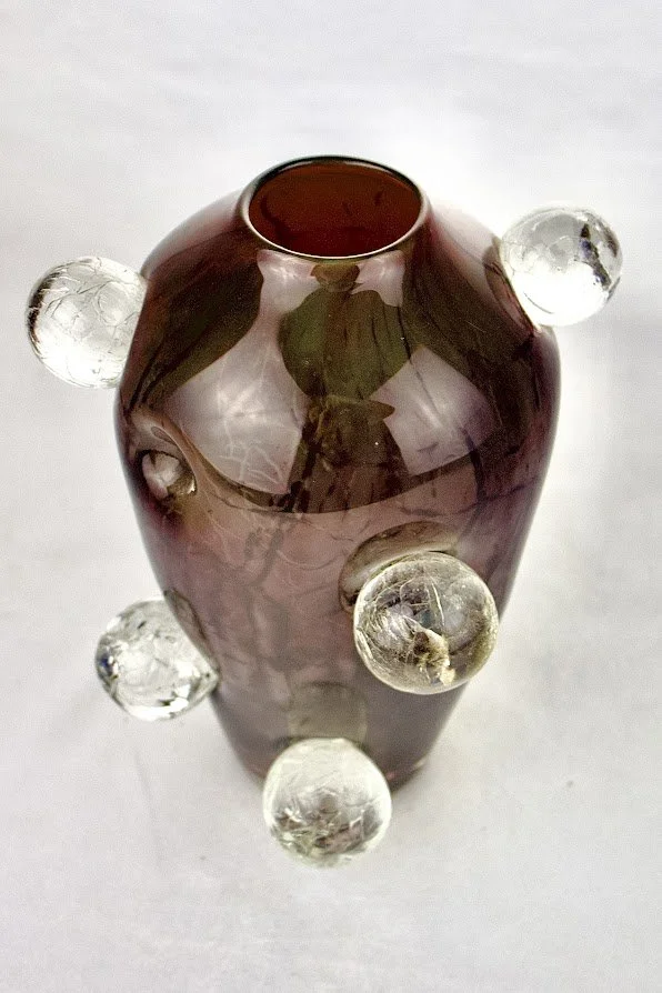 A decorative glass vase with a dark pink body and clear glass spheres attached to its sides.