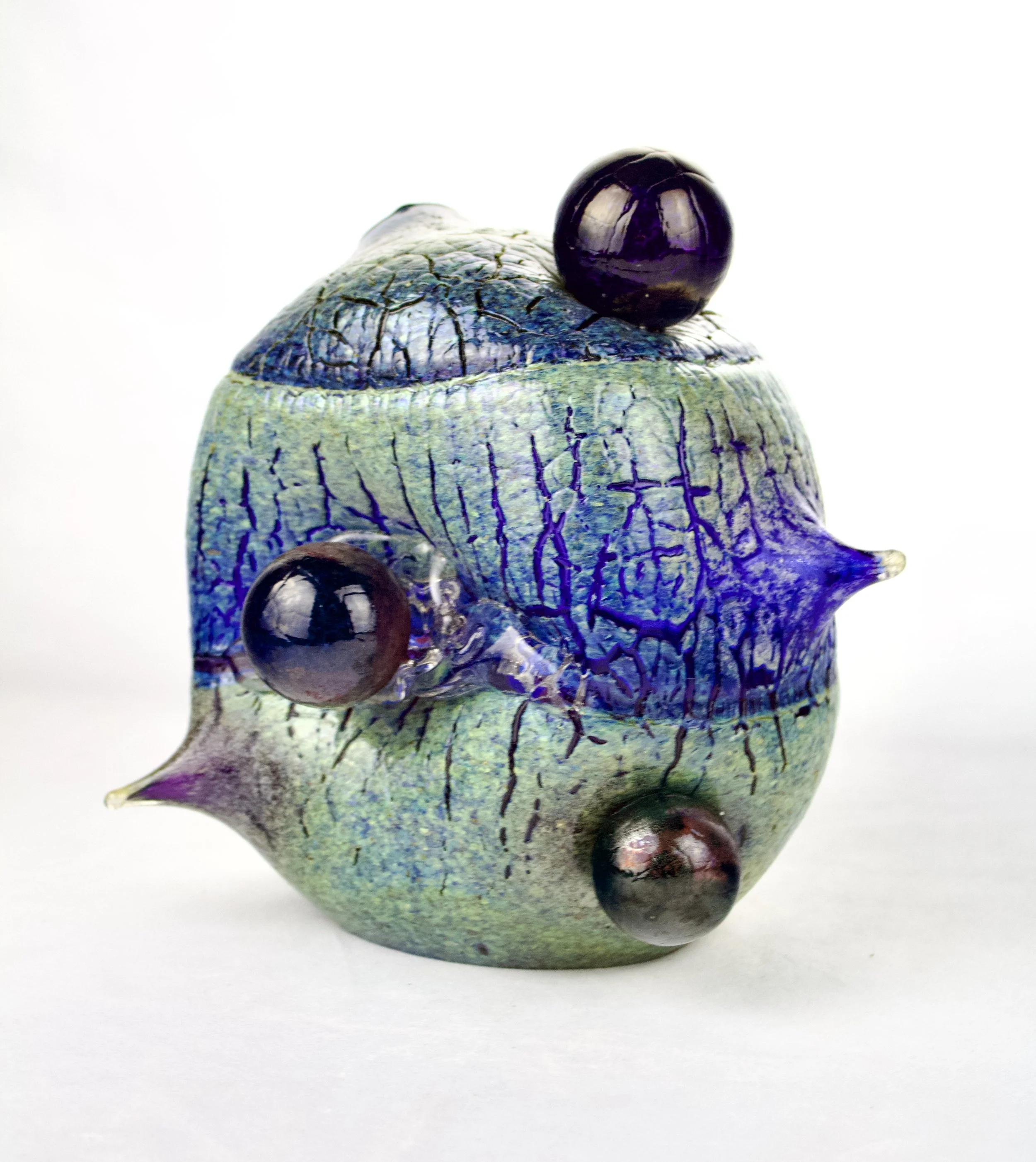Colorful, abstract glass sculpture with a green, blue, and purple cracked surface and four spherical protrusions.
