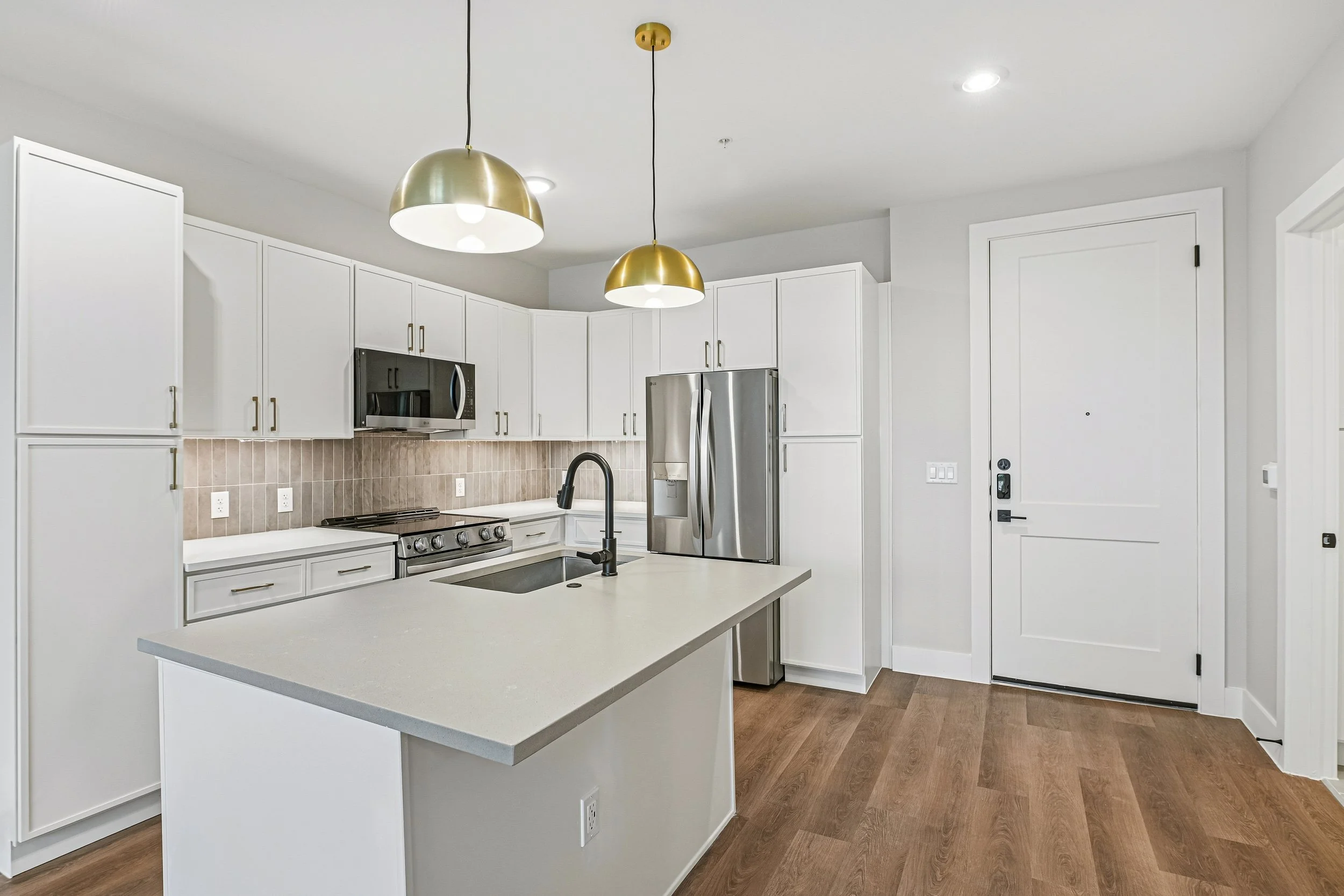 Modern kitchen with white cabinets, a central island, stainless steel appliances, pendant lights, and wood flooring.