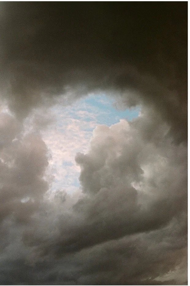 Dark storm clouds with an opening revealing a patch of blue sky and light-colored clouds.