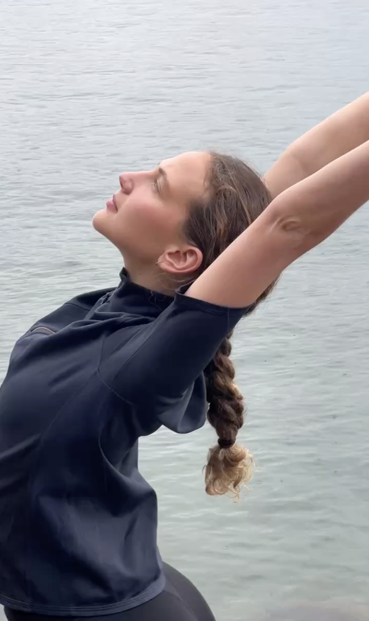 Woman stretching beside the ocean during an outdoor movement practice