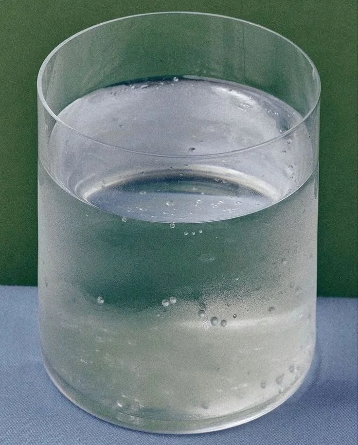 A transparent glass filled with water and carbon dioxide bubbles, placed on a surface with a green background.