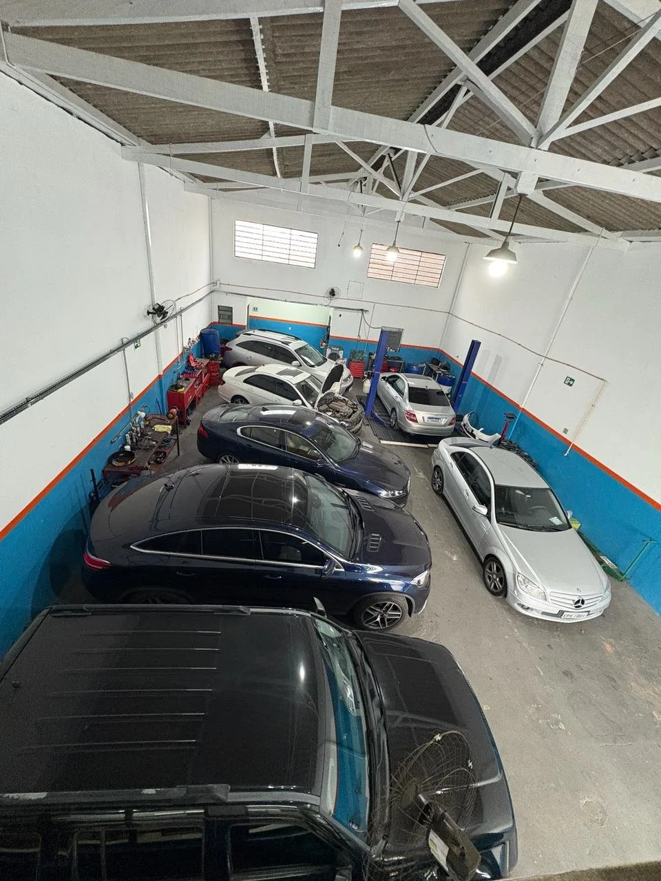 Vários carros estacionados dentro de uma oficina de manutenção automotiva, com ferramentas e equipamentos ao fundo.