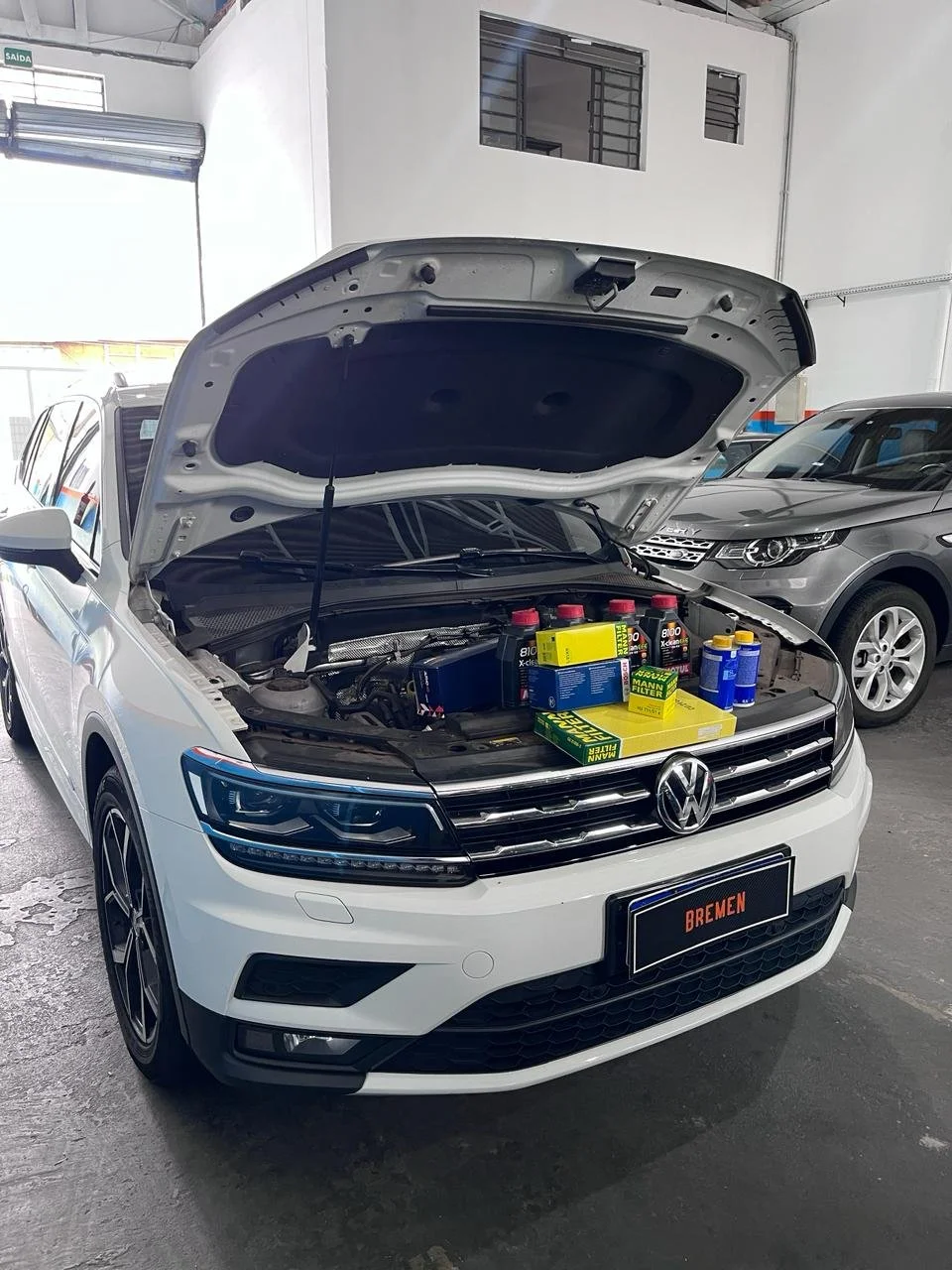 Carro Volkswagen com o capô aberto, com várias peças de reposição e filtros na tampa do motor, em uma oficina garagem.