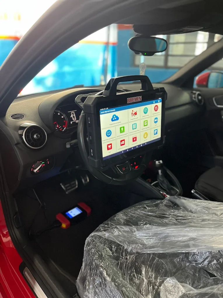 Interior de um carro com um dispositivo de diagnóstico conectado ao painel, exibindo uma tela com vários ícones e uma marca de 'Bremen' na parte superior.