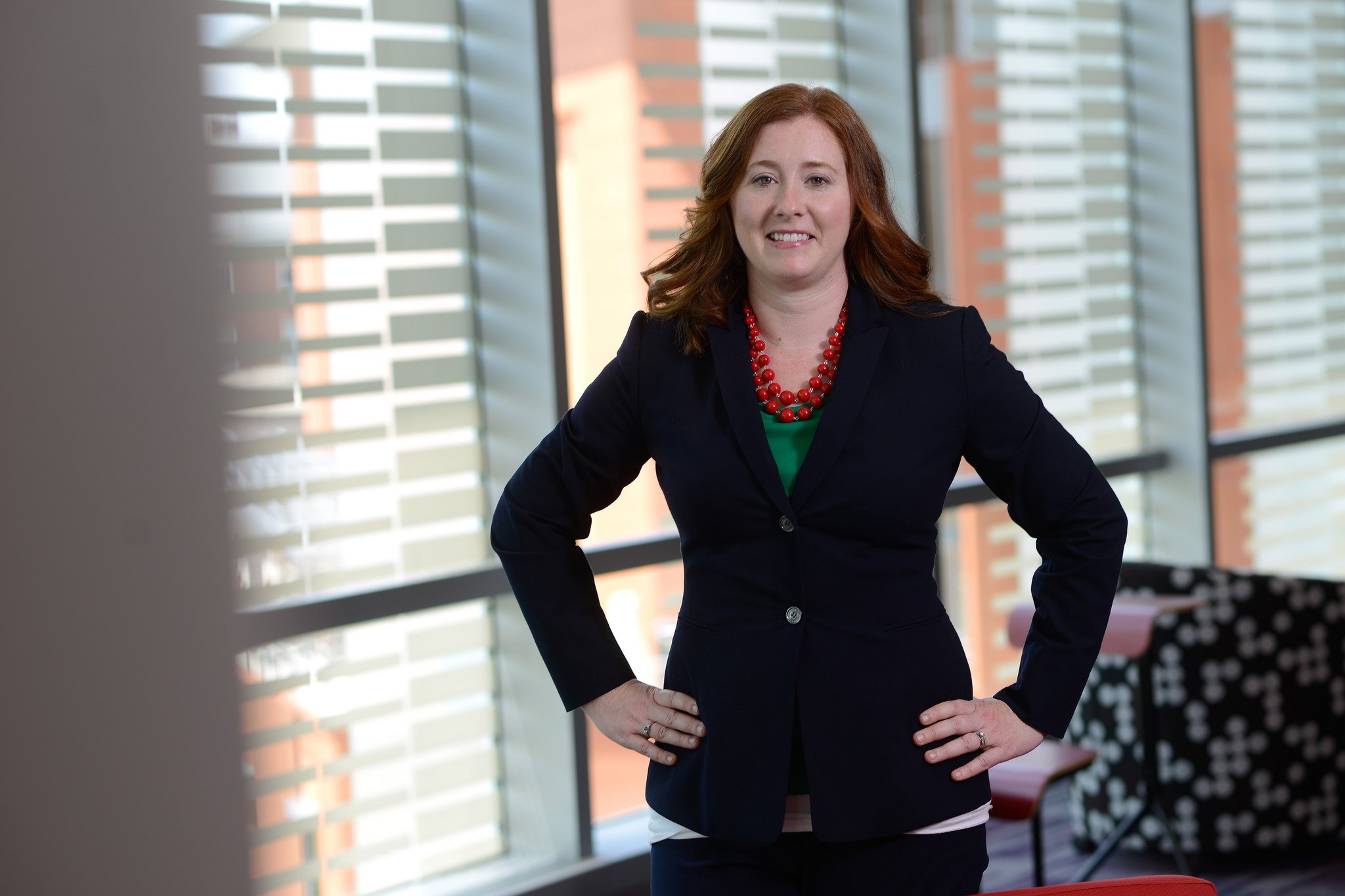 Red-haired woman in a business suit standing confidently in a modern office building.