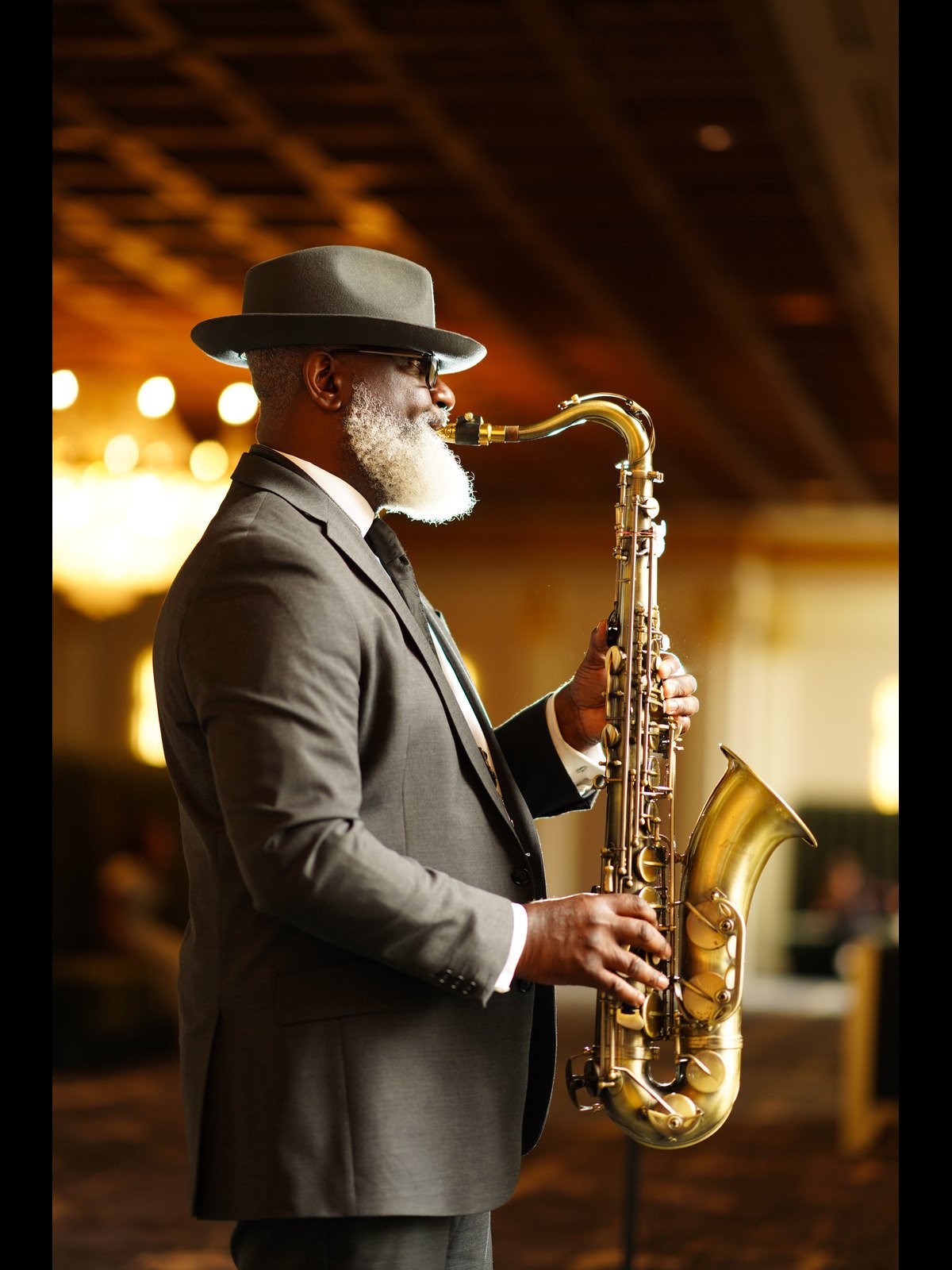 A professional saxophonist performing live saxophone music at an indoor event in a warmly lit space.