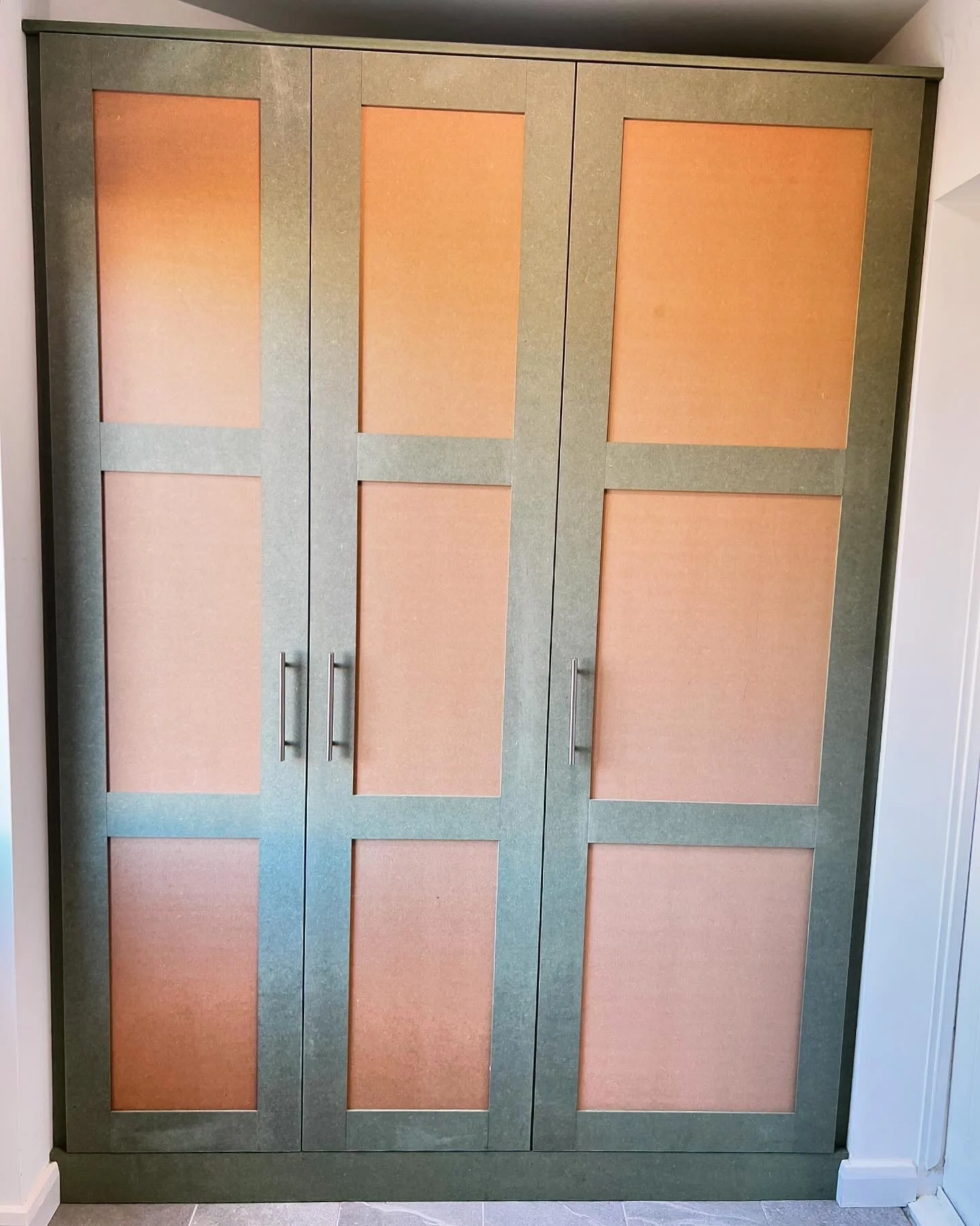 A large green cabinet with six pinkish-brown doors, each with silver handles, situated against a wall.