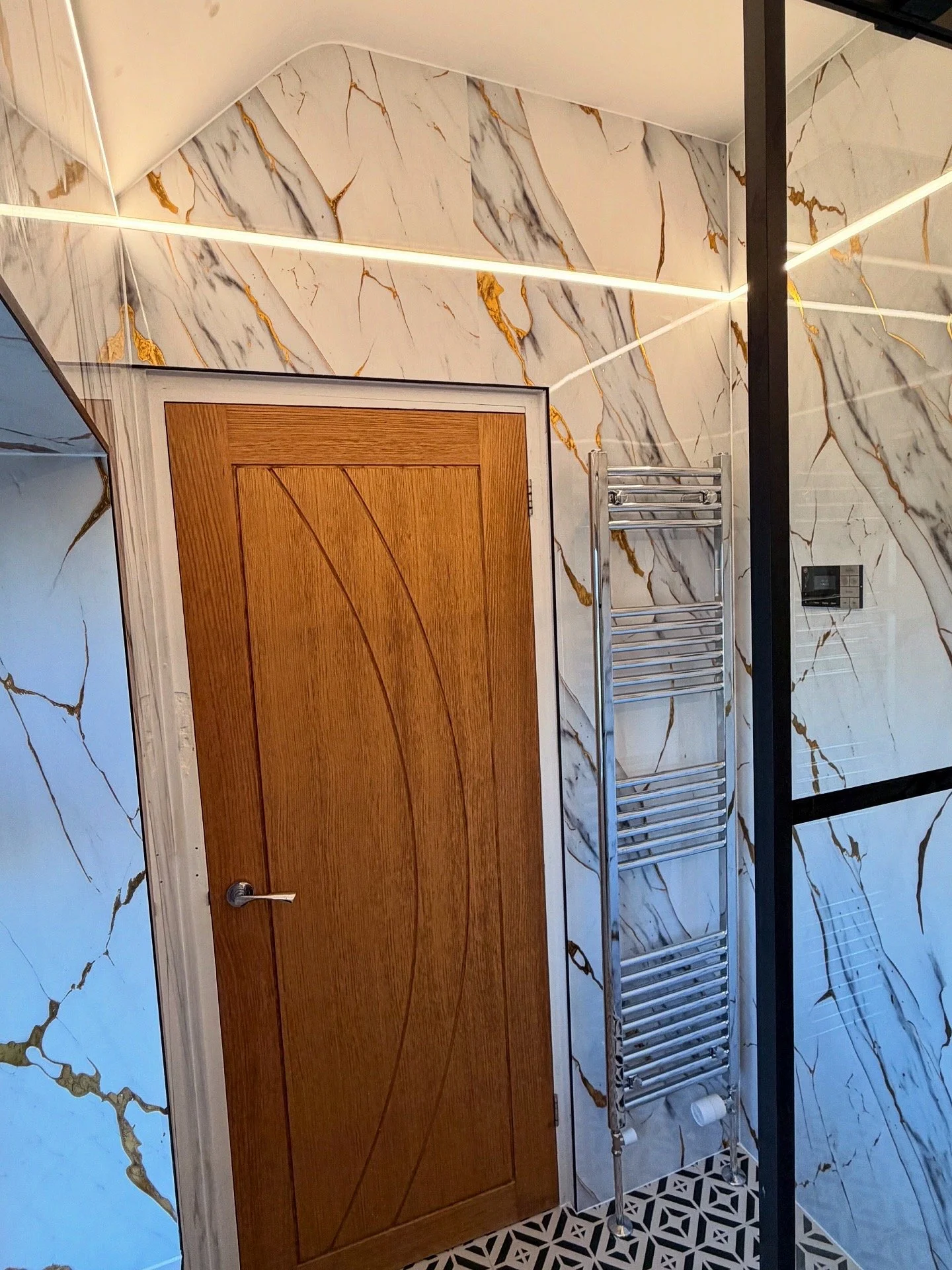 Interior view of a bathroom with marble-patterned walls, a wooden door, and a stainless steel towel rack.