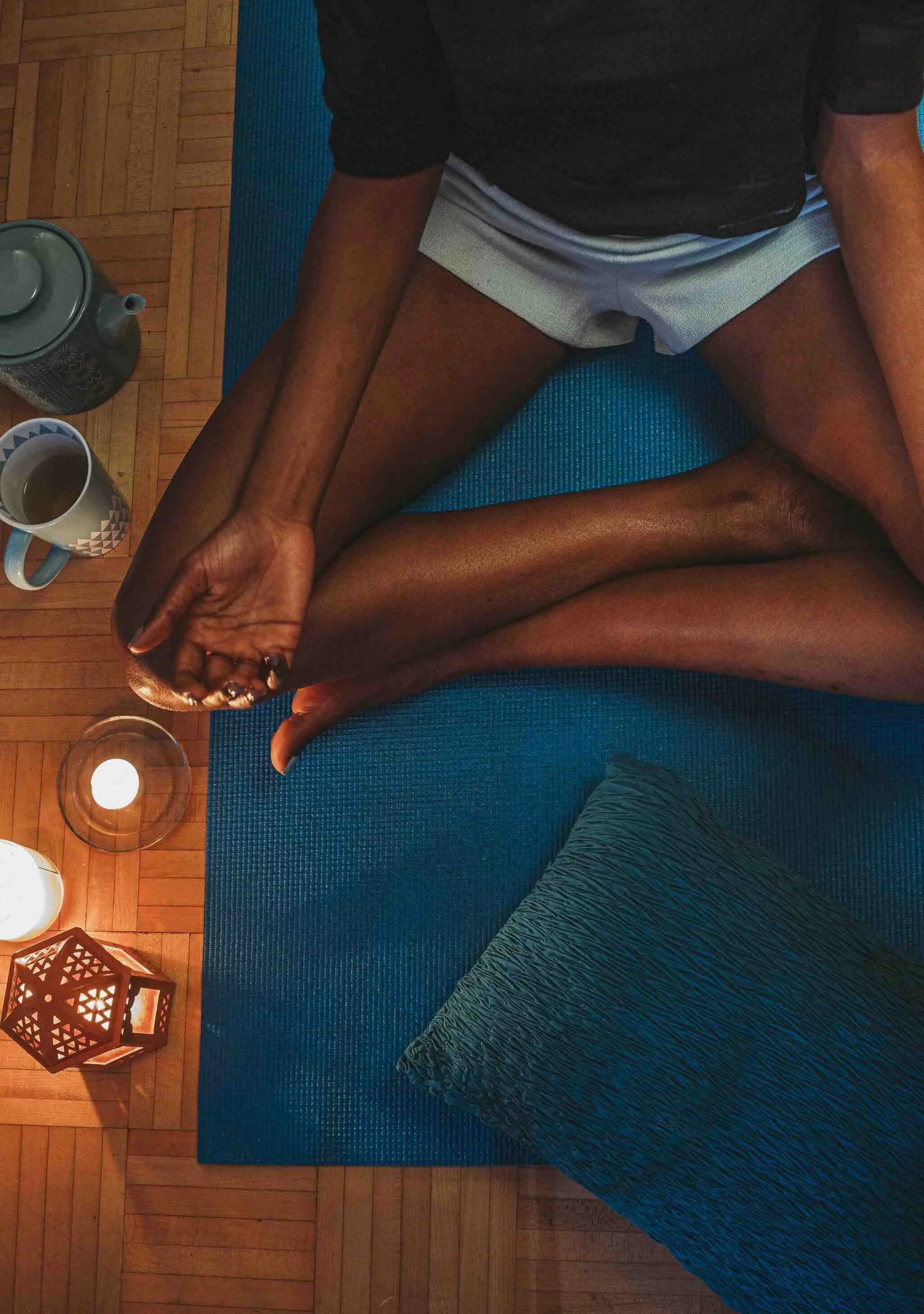 Person méditant assis en tailleur sur un tapis bleu, dans une ambiance chaleureuse avec des bougies et une lampe en bois.