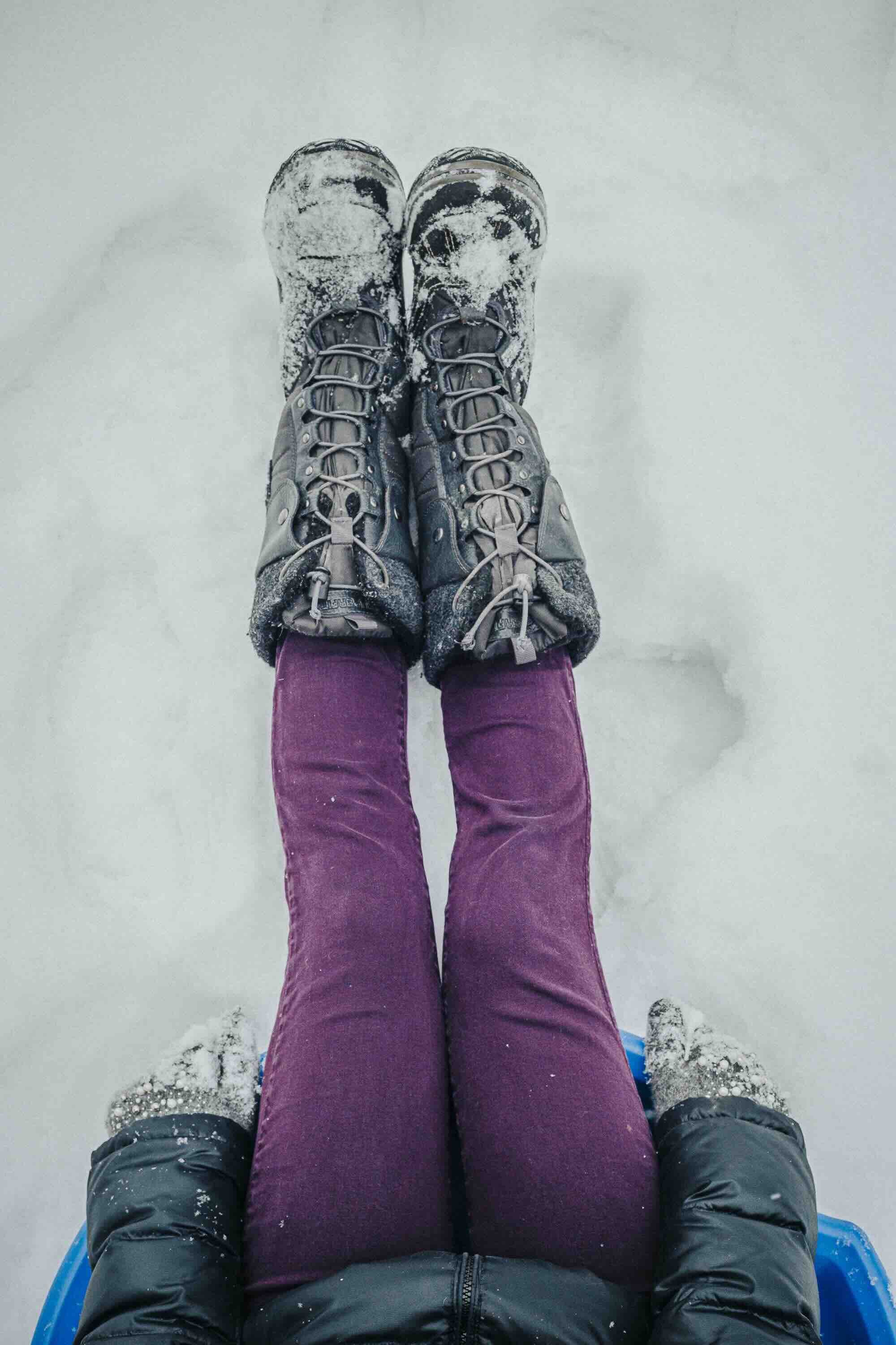 Deux personnes portant des bottes de randonnée, prises en photo du point de vue de leurs pieds dans la neige, avec des vêtements d'hiver visibles.
