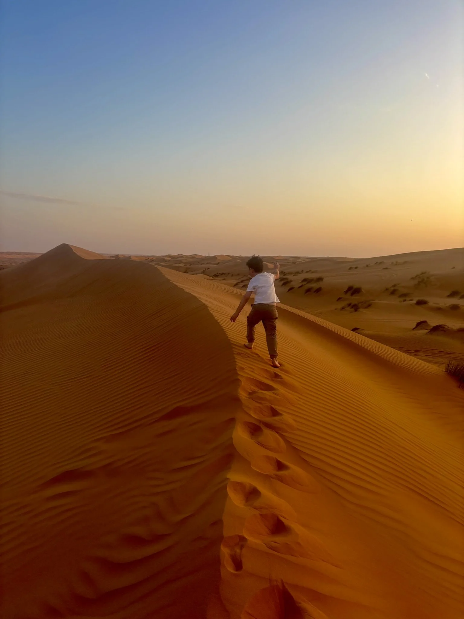 Child walking on sand dunes during sunset in the Wahiba Sands desert in Oman.