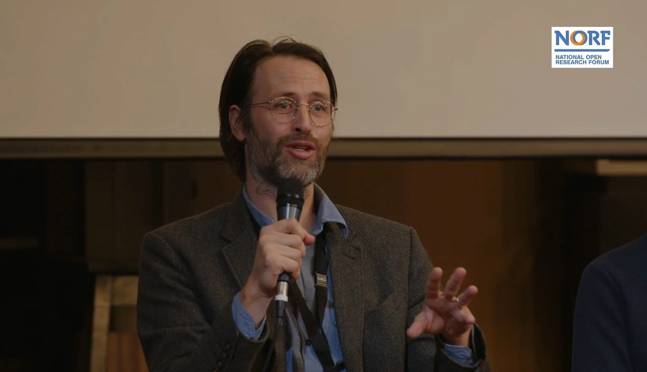 Christopher Loughnane, a speaker at the National Open Research Forum (NORF), speaks into a microphone during a panel discussion.