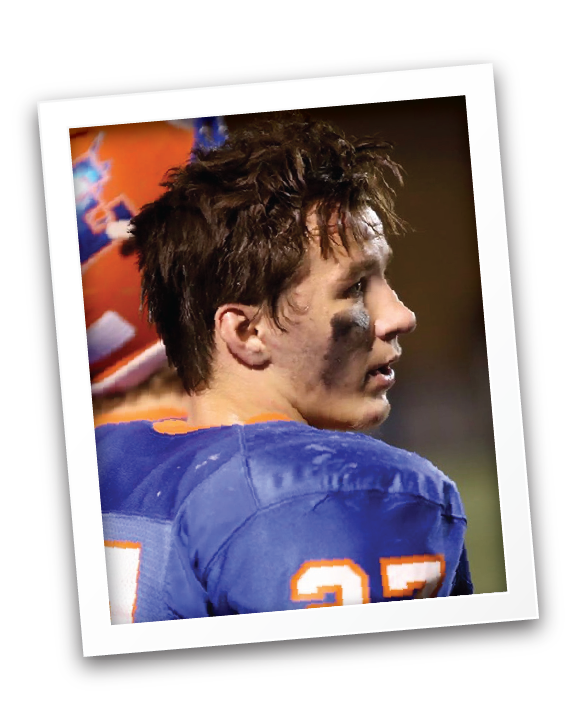 Close-up of Max in a blue jersey with the number 27, looking to the side with dirt on his face, after a football game.
