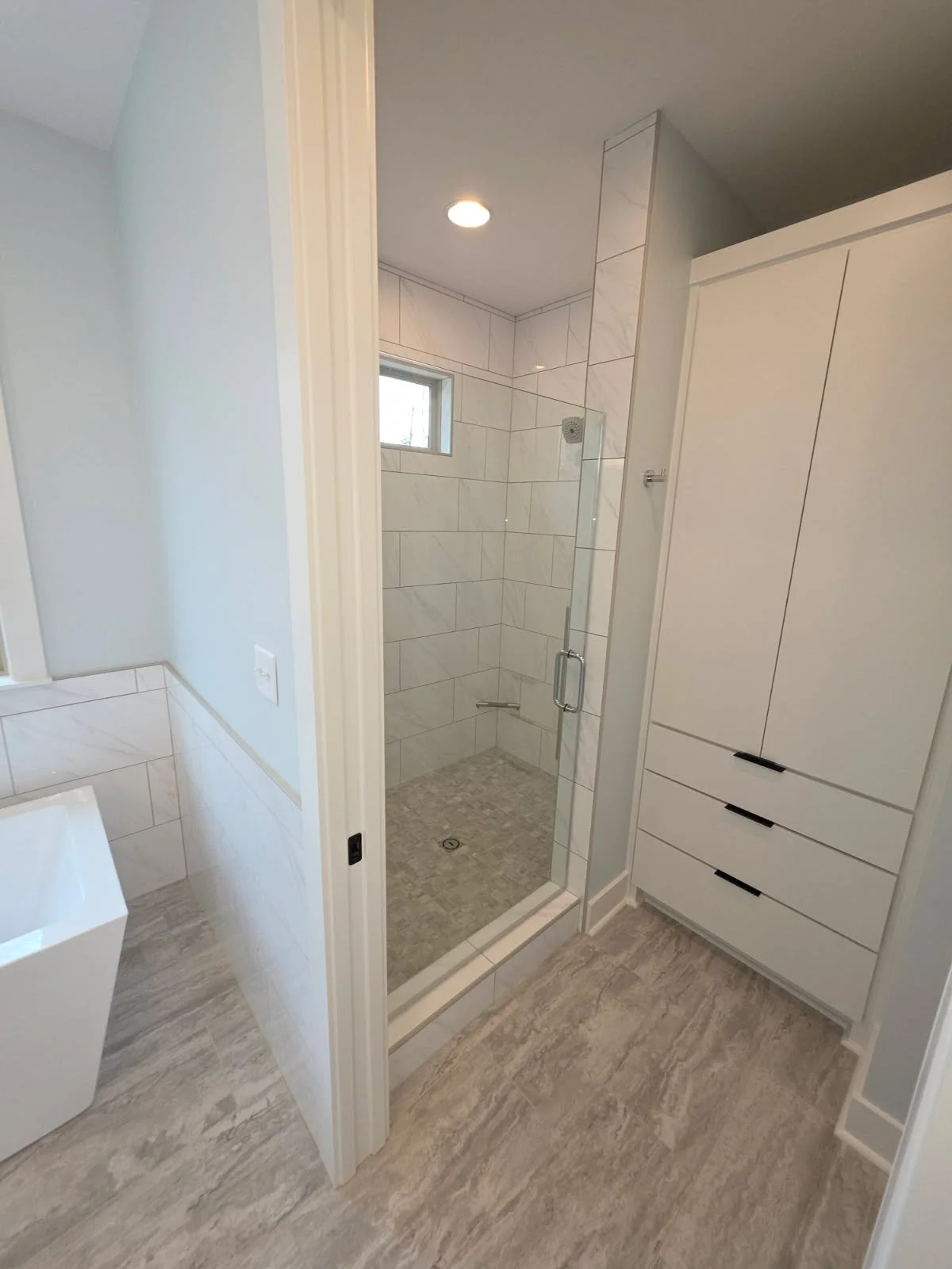 Bathroom with a shower, a small window, and white cabinetry.