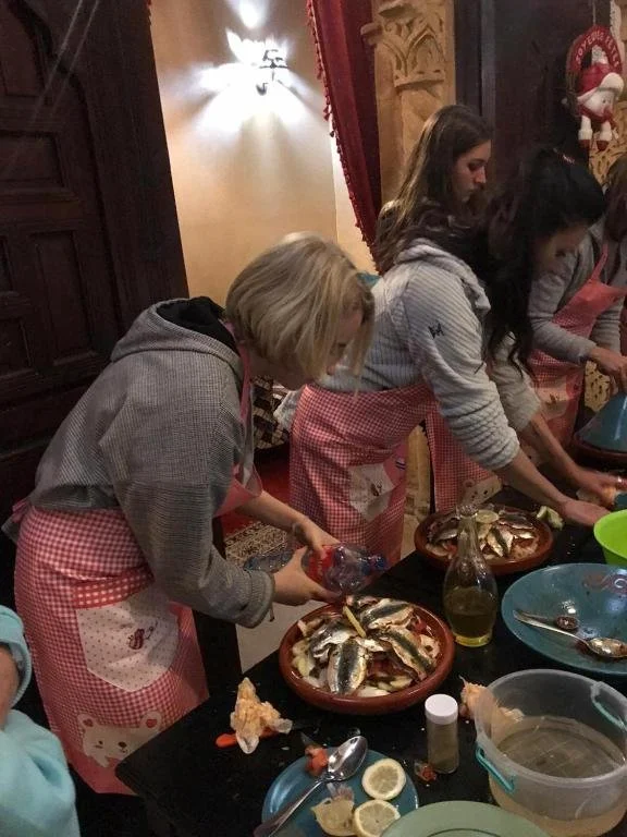 Un groupe de jeunes femmes préparant un plat à base de poisson dans une cuisine ou une salle à manger décorée pour Noël.