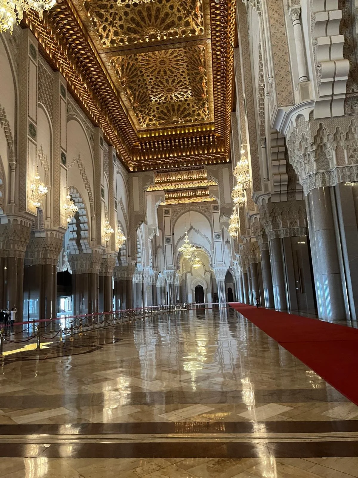 Intérieur d'une grande salle luxueuse avec un plafond orné, chandeliers chandeliers et colonnes décoratives, un tapis rouge sur le sol en marbre brillant.