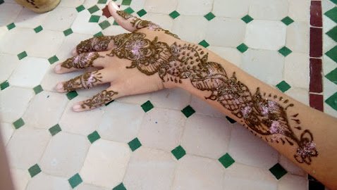 Main droite posée sur un sol en carreaux de céramique, avec des motifs d'henna décoratifs sur la main et le bras.