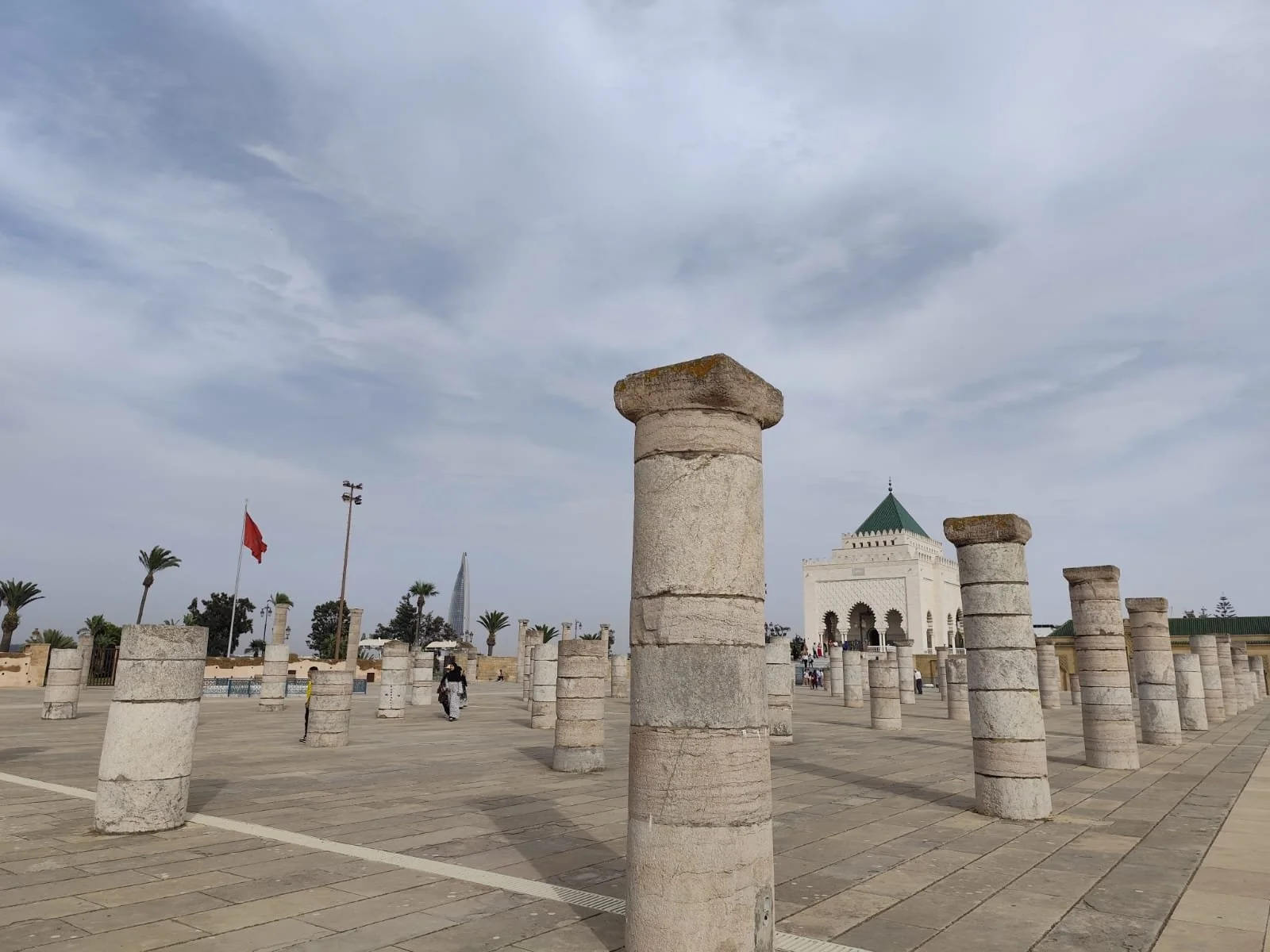 Vue du centre-ville de Marrakech avec des colonnes en pierre et un monument blanc avec un toit vert, sous un ciel nuageux.