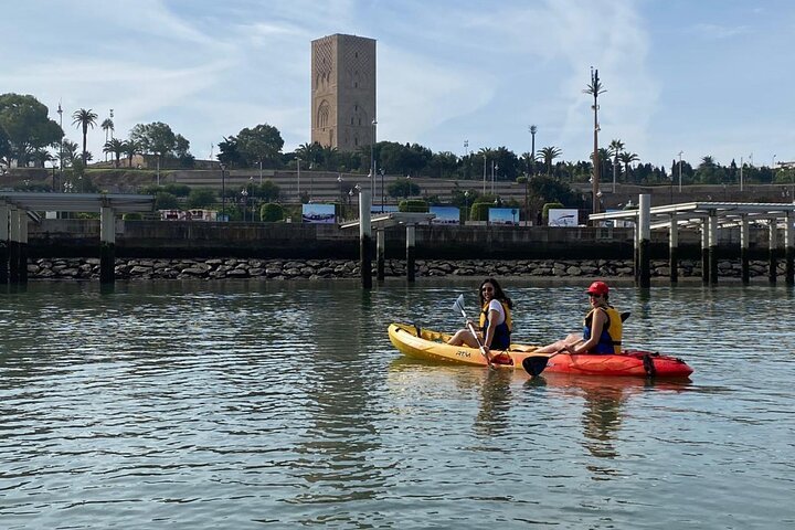 Deux personnes faisant du kayak sur la rivière avec la tour Hassan en arrière-plan, dans une ville marocaine.