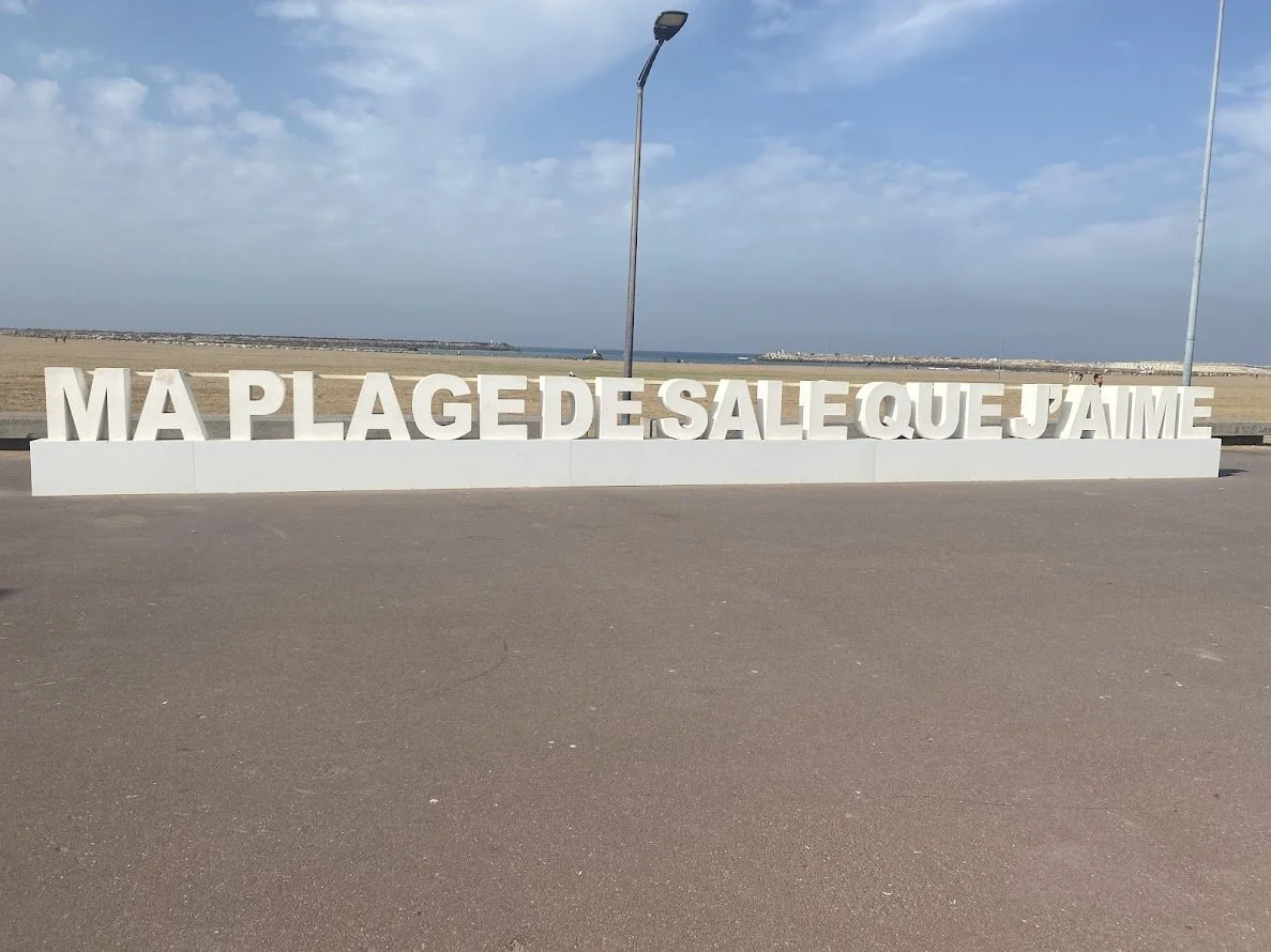 Message en lettres blanches sur la promenade, disant 'Ma plage de sable que j'aime', avec la plage et la mer en arrière-plan.