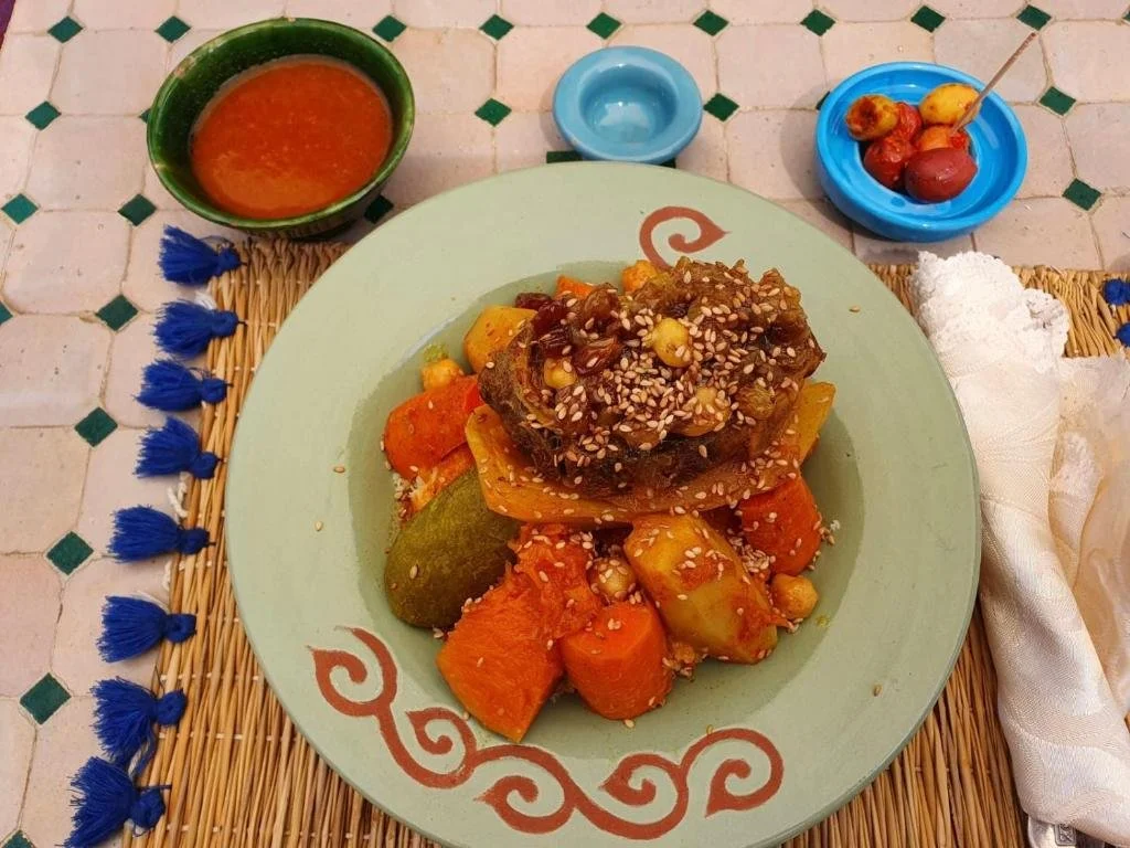 Assiette de ragoût marocain avec légumes comme carottes, courgettes et pommes de terre, garnie de graines de sésame, accompagnée de sauce tomate et de fruits confits.