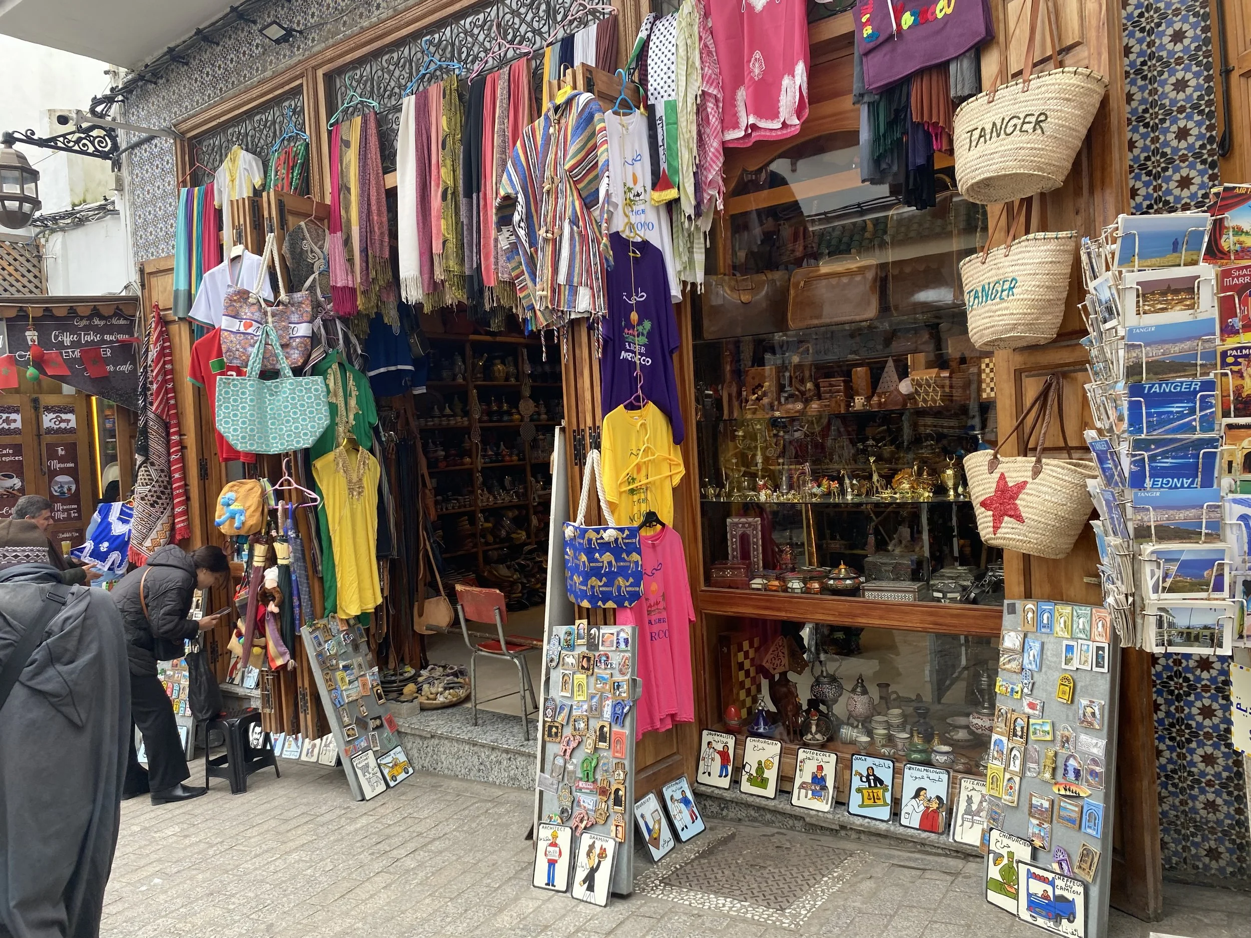 Magasin de souvenirs et vêtements à Tanger, Maroc, avec des sacs, vêtements colorés, et des souvenirs en vitrine.