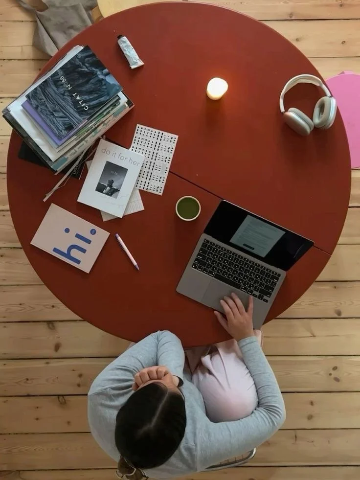 A workspace with a MacBook Pro laptop displaying the text 'Workhard Anywhere', a black smartphone, a white Apple Magic Mouse, a white plant pot with a green grass plant, a black closed notebook, and a white background.