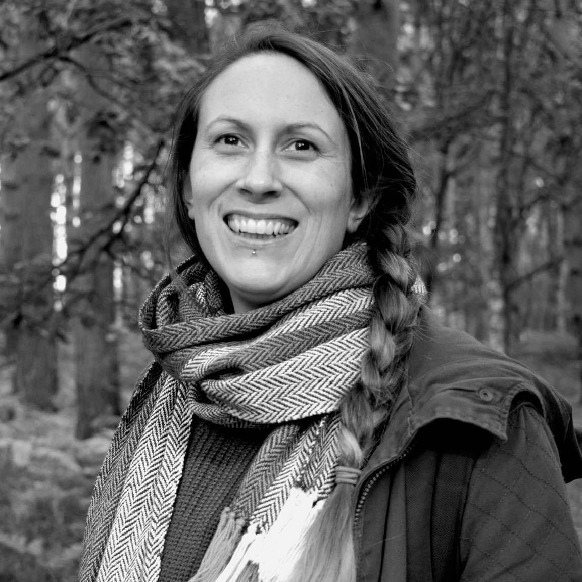 black and white photo of a white woman smiling and looking off camera with woodland in the background