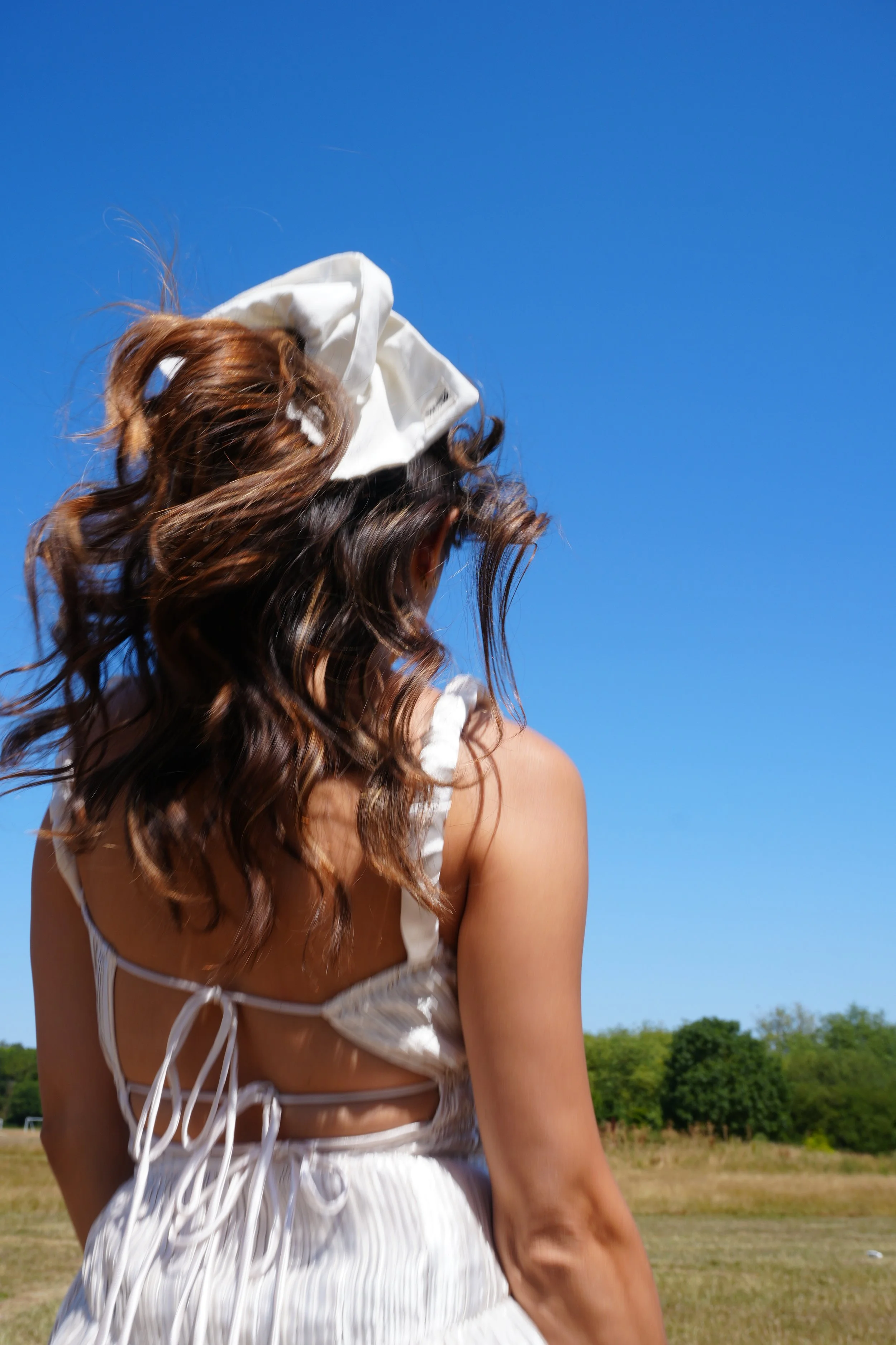 A woman with long wavy brown hair wearing a white SquareBand tied-up top