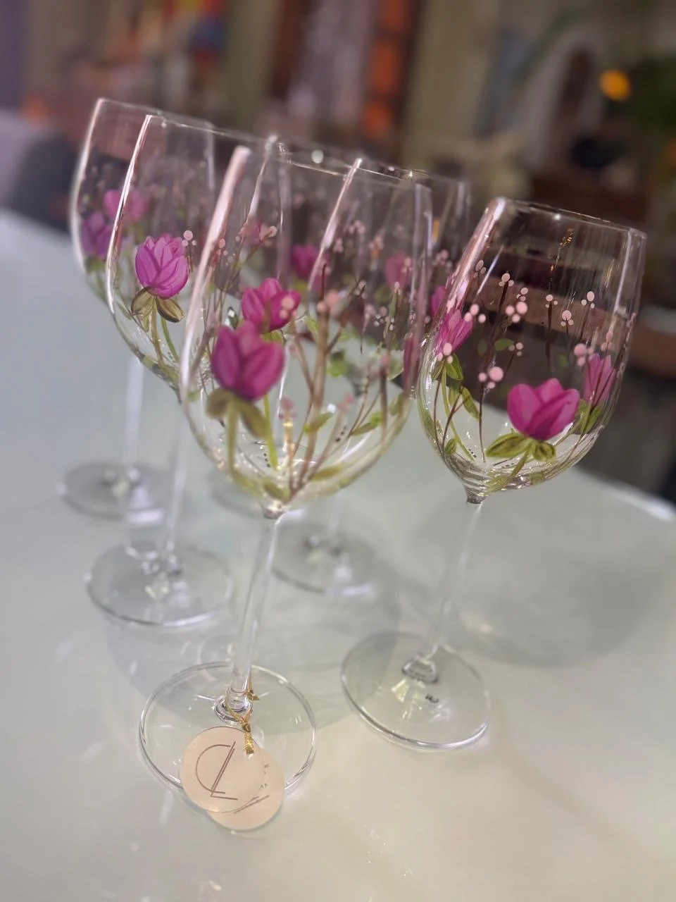 Vasos de vidro com flores rosas pintadas em estilo delicado, dispostos em fila sobre uma mesa branca