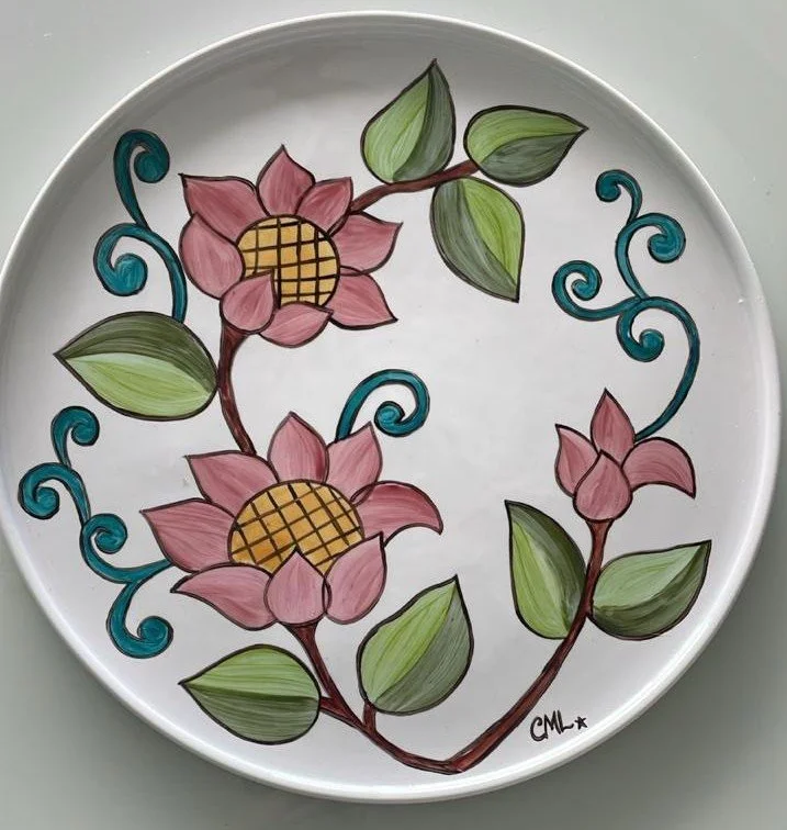 Prato decorado com flores de galhos com folhas verdes, detalhes azuis e flores rosa com centros amarelos. Assinatura CML no canto inferior direito.