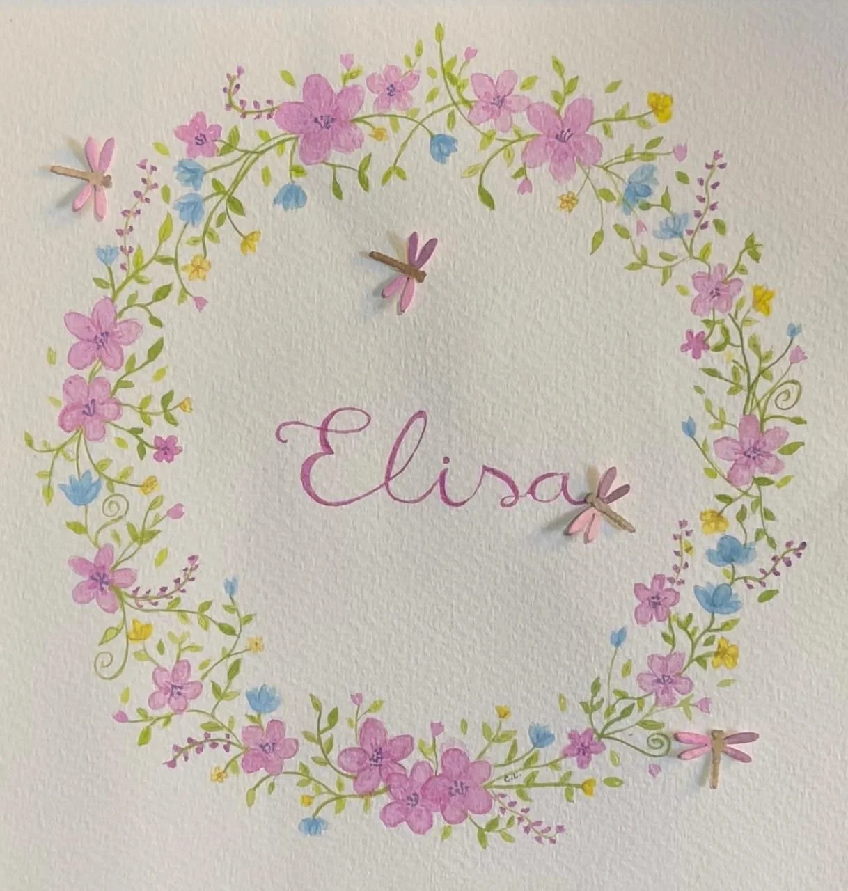 Quadro decorativo com flores em tons de rosa, azul e amarelo formando um círculo, com a palavra 'Elisa' ao centro escrita em letra cursiva rosa.