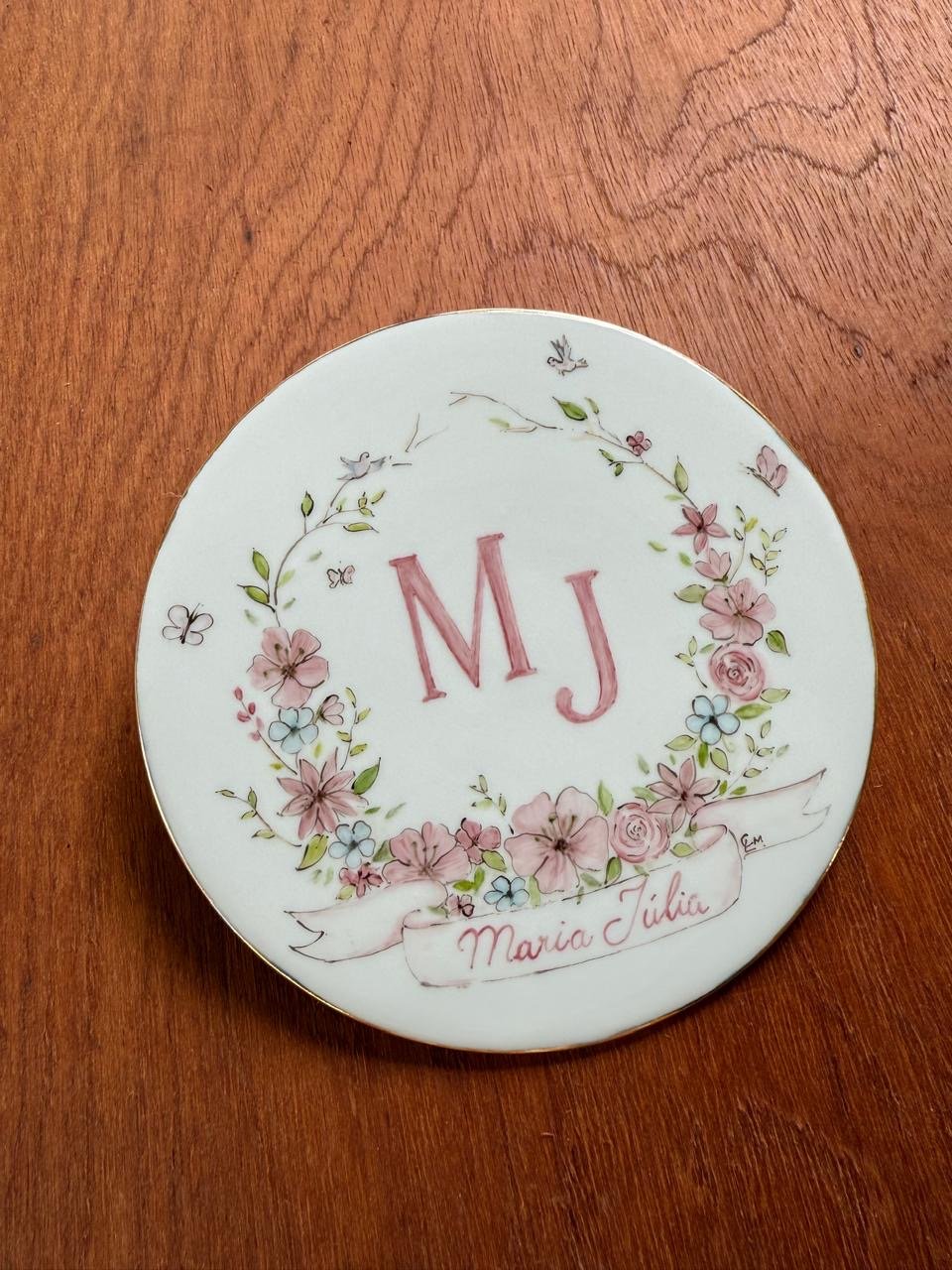 Prato decorativo com as iniciais MJ e o nome Maria Júlia, rodeado por um buquê de flores e borboletas em cores suaves.
