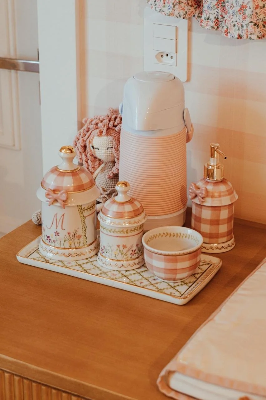 Conjunto de utensílios de banheiro decorados com padrão xadrez em cores suaves, incluindo um saboneteira, uma caixinha, uma tigela e um recipiente com bomba de sabonete, dispostos sobre uma bandeja em cima de uma mesa de madeira.