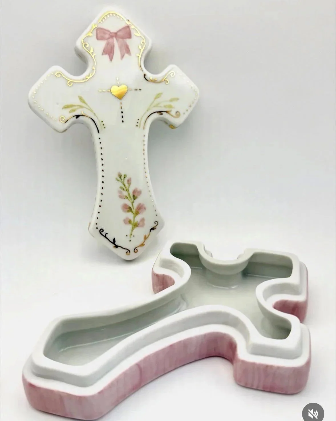 Cruz de cerâmica decorada com detalhes dourados, rosa e verdes, acompanhada por moldes de cortador de biscoito com forma de cruz, ambos sobre fundo branco.