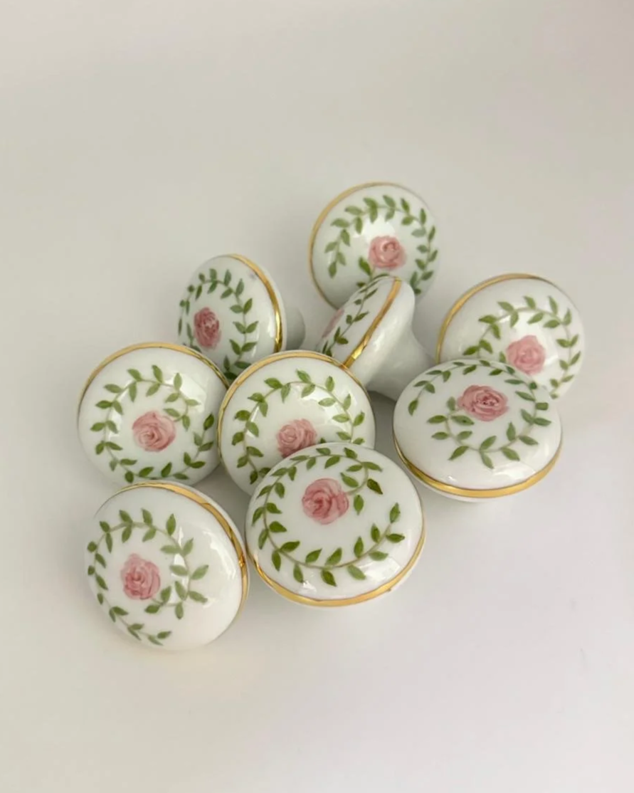 Conjunto de botões decorativos brancos com detalhes de rosas rosa e folhas verdes em volta, com acabamento dourado nas bordas.