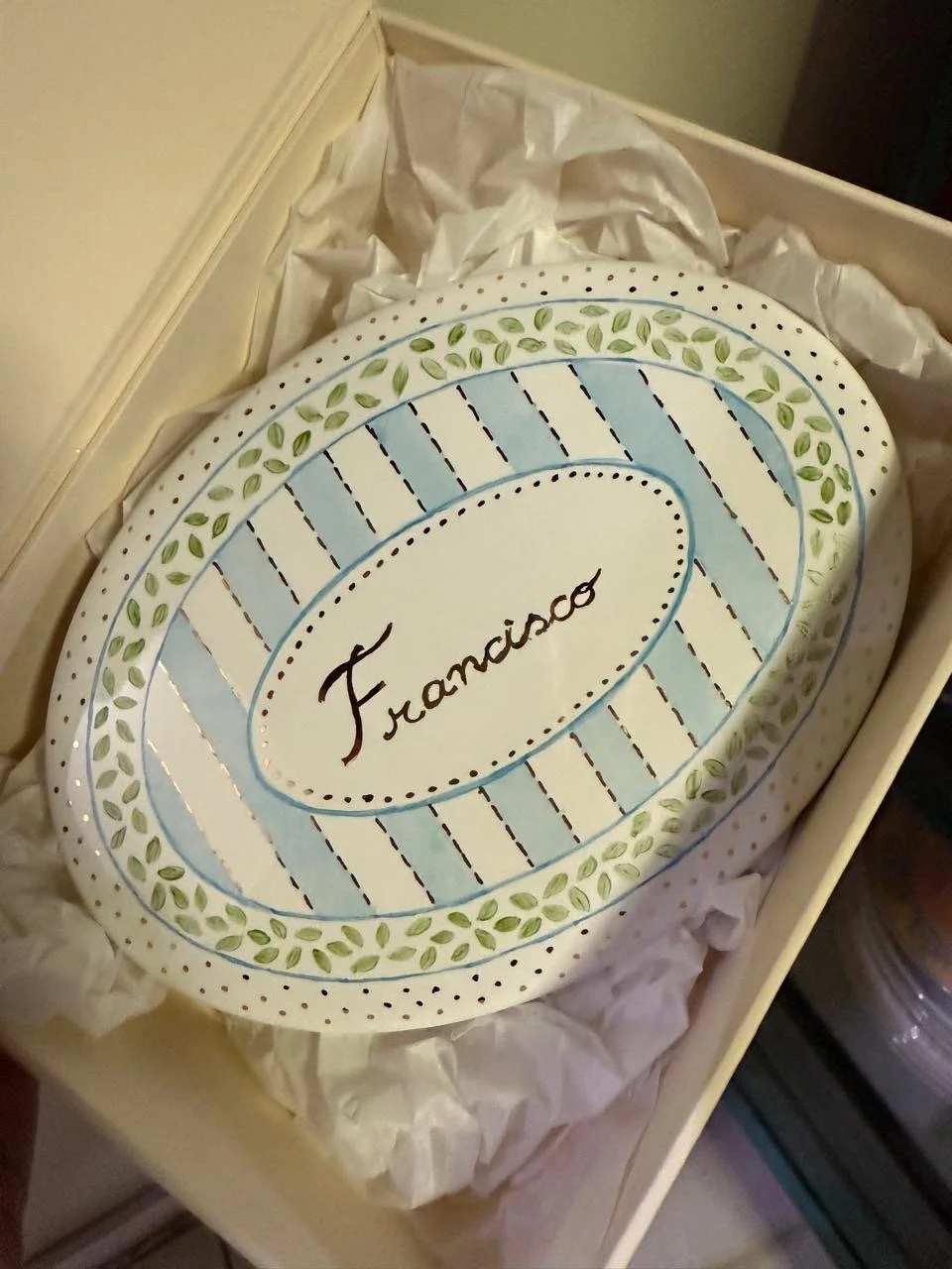 Coração decorativo com a palavra 'Francisco' escrita, em cores suaves de azul, verde e branco, em uma caixa com papel de seda branco.