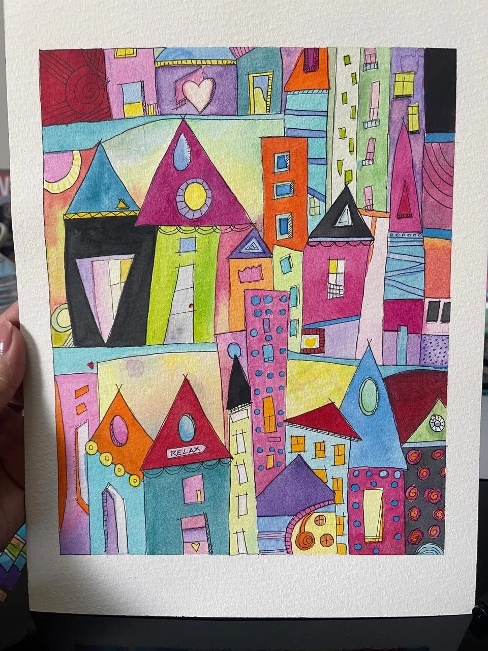 Desenho de uma cidade colorida com edifícios e casas com telhados pontudos em vários tons e formas, incluindo algumas com detalhes decorativos e palavras como 'RELAX'.