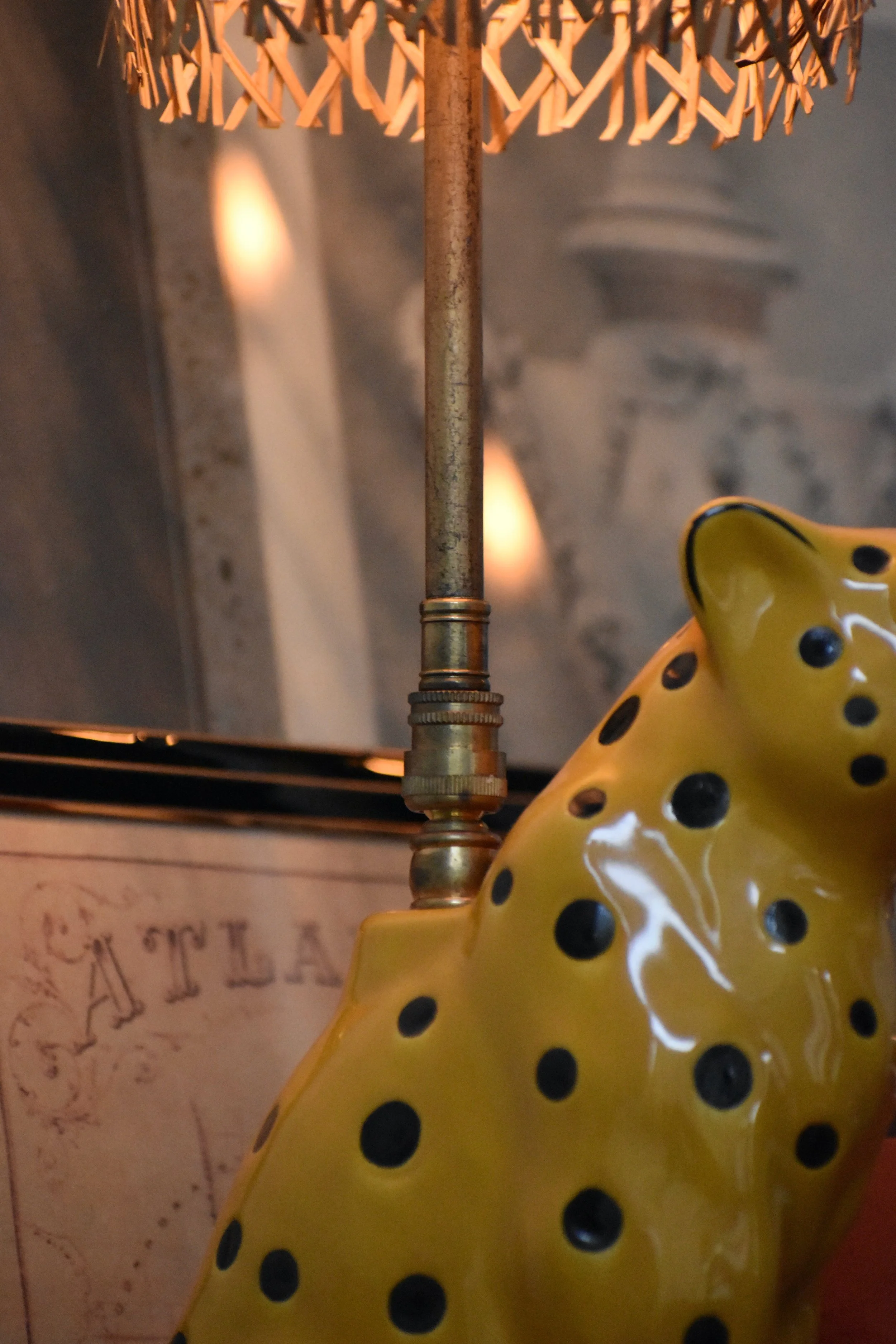 Close-up of a decorative yellow ceramic object with black polka dots, a brass rod, and a wicker lamp in the background.