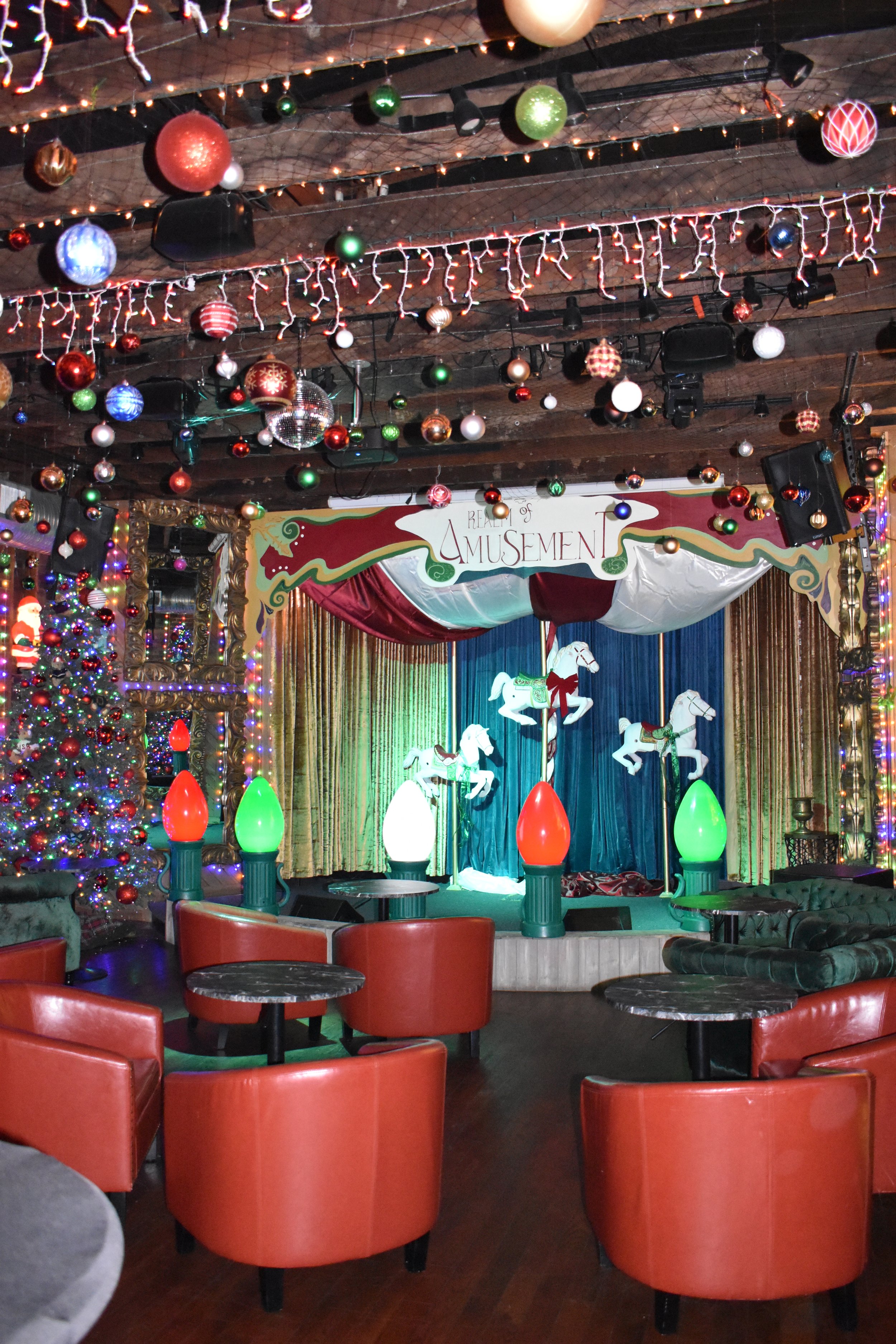 Decorated indoor amusement stage with Christmas ornaments, Christmas tree, colorful lights, and a sign reading 'Revel of Amusement'