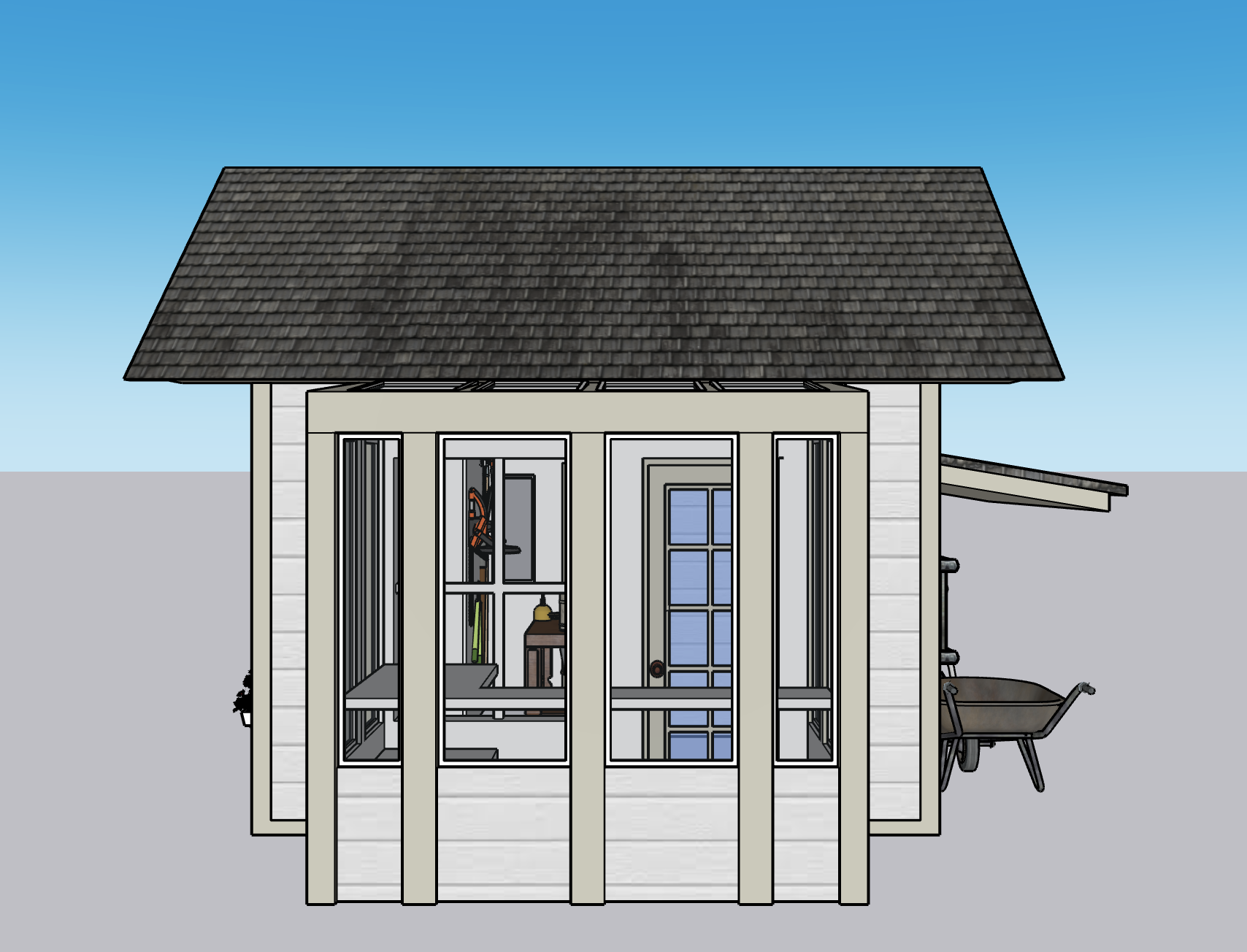 A small gray and white shed with a dark shingled gable roof, glass door, and windows, with a wheelbarrow tucked on the right side.