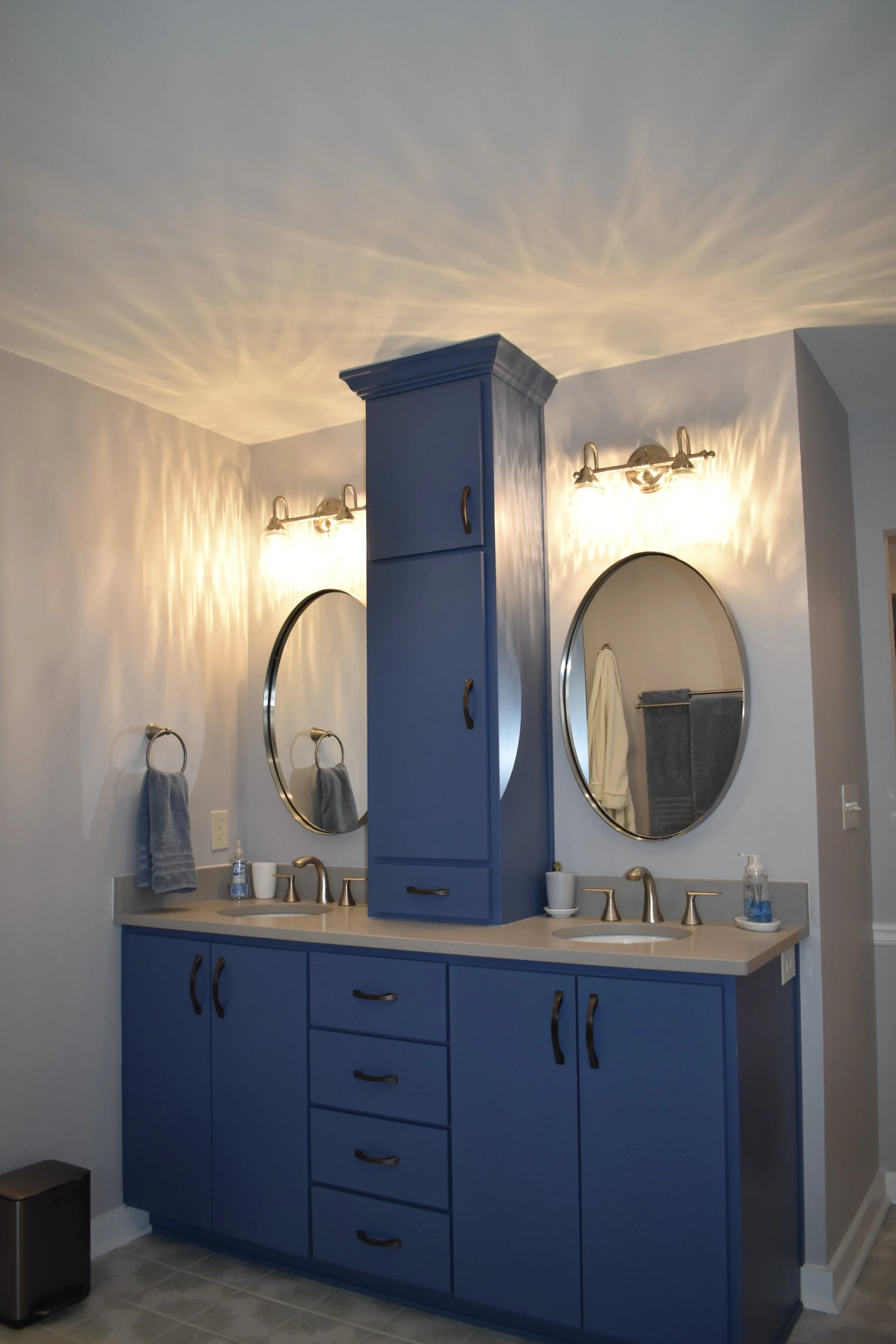 Double bathroom vanity with blue cabinets, beige countertop, two oval mirrors, and lighting fixtures, with towels and toiletries visible. Marietta GA bathroom remodel.