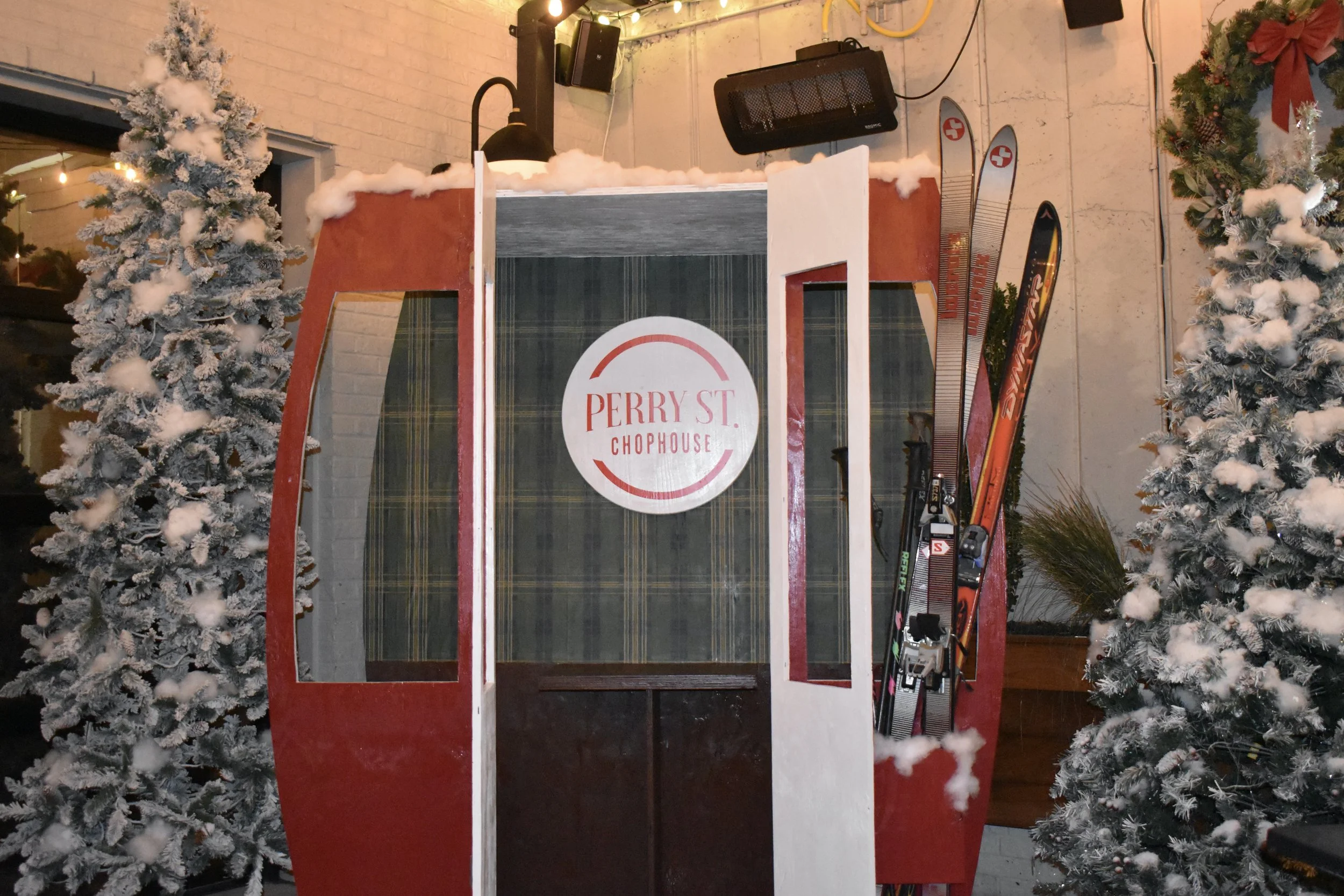 A snow-covered ski lift gondola at Perry Street Chophouse, decorated with Christmas trees and holiday decor.