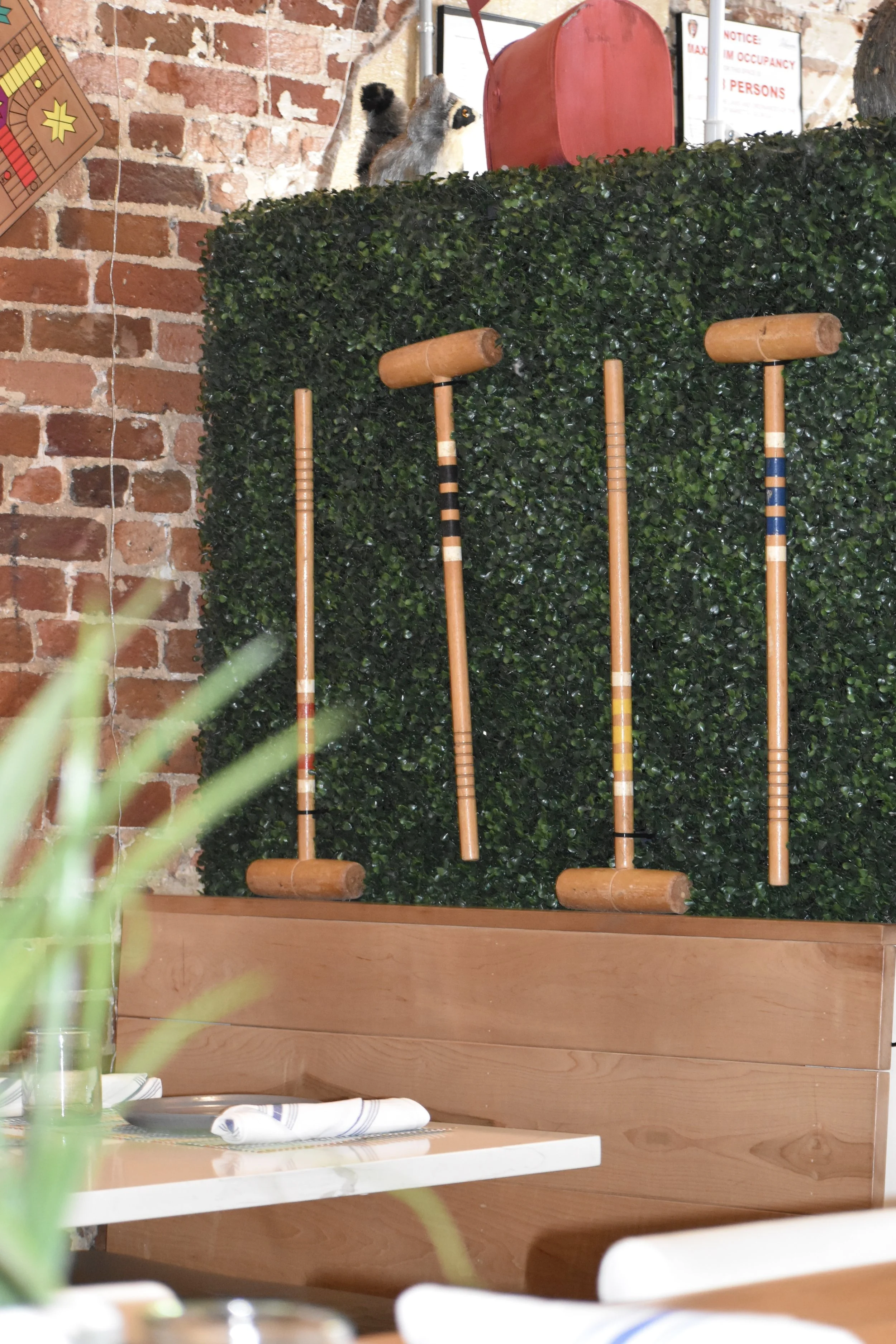 Interior of a restaurant with decorative gaming sticks on a green hedge wall and a brick wall in the background. Hamp & Harry's Marietta Square.