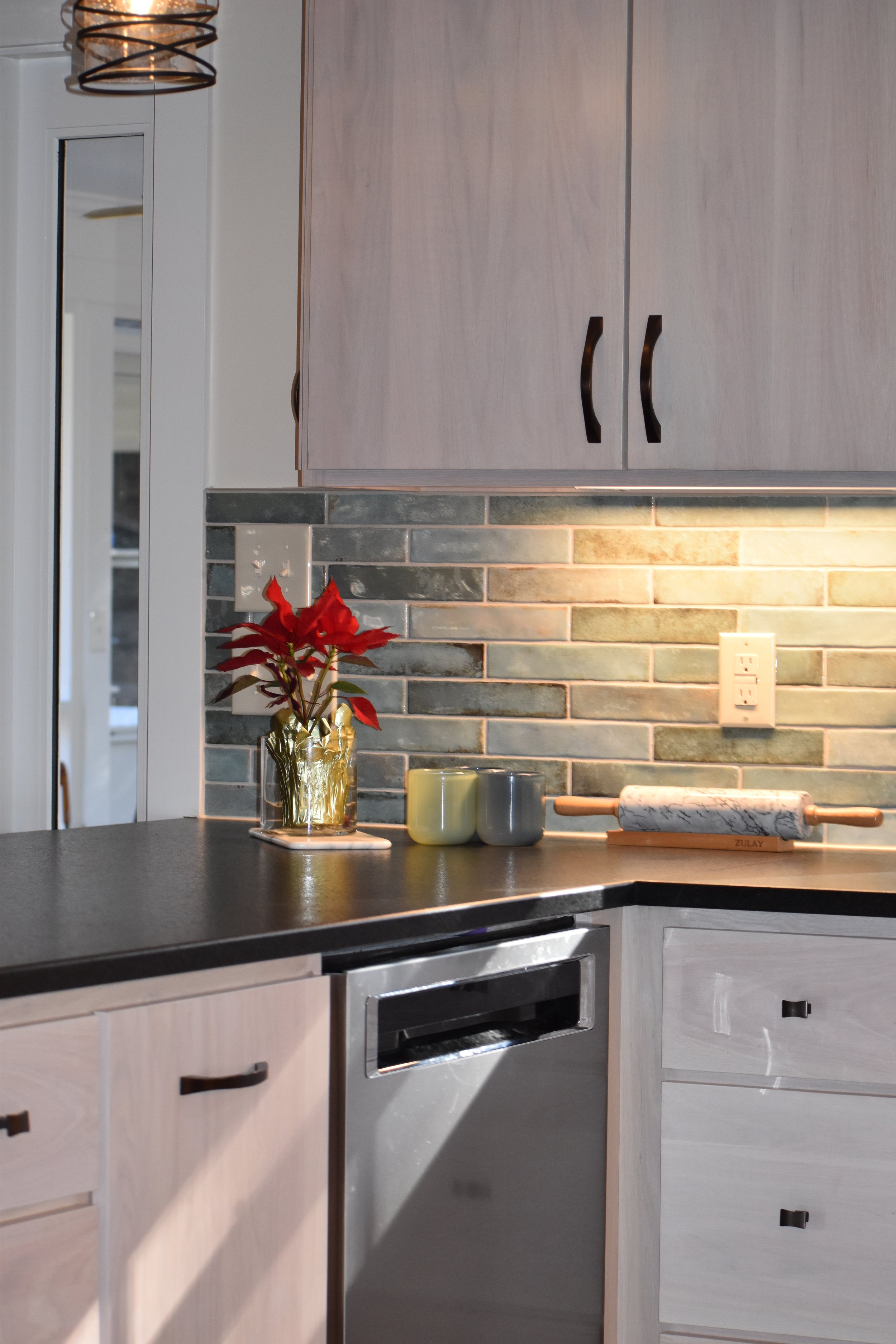 A kitchen countertop with a potted red poinsettia plant, two candles, and a marble rolling pin. The background features a brick backsplash, cabinets, and a light switch. Marietta GA kitchen remodel.