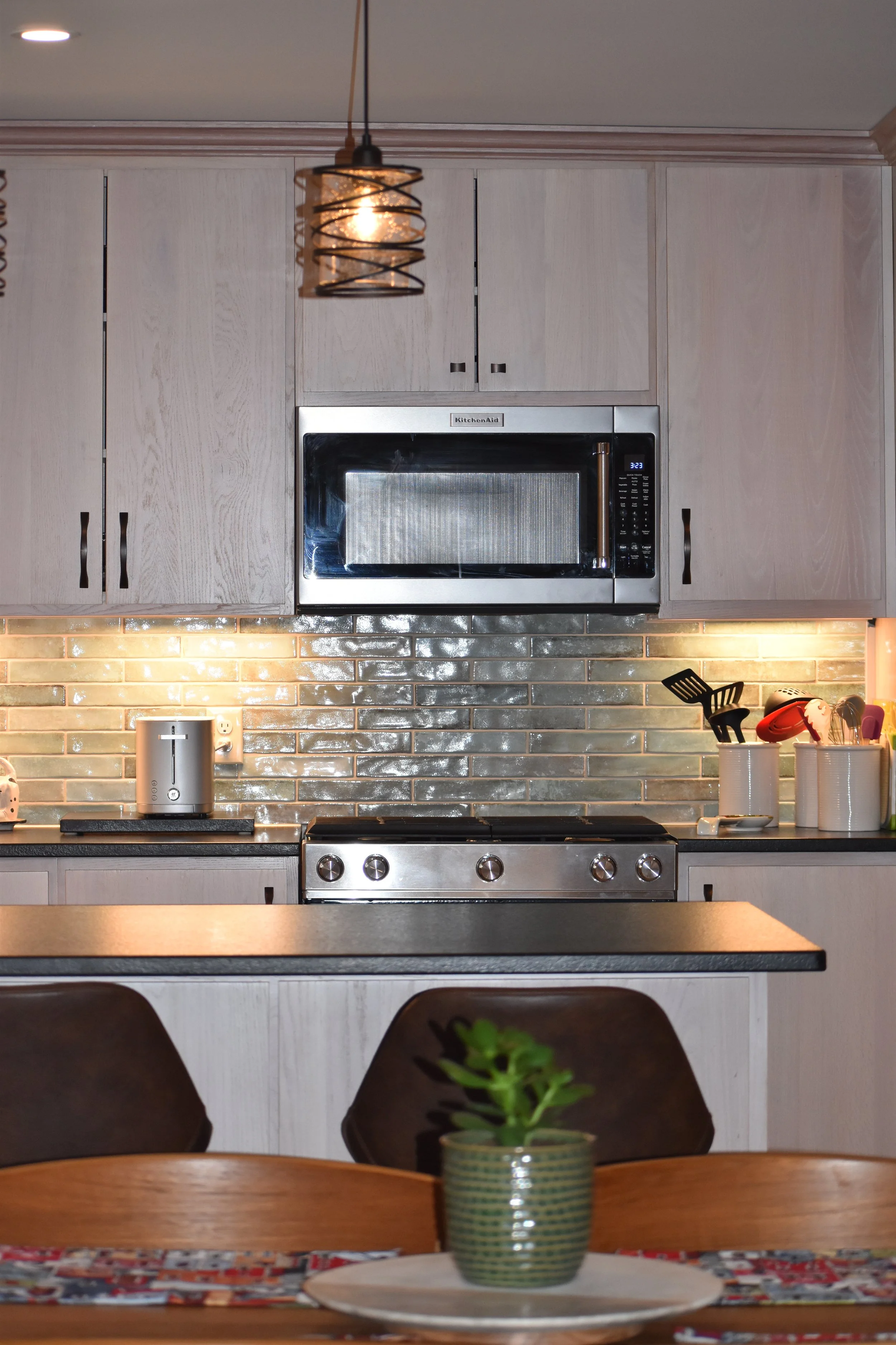 Kitchen with a microwave oven above a stove, a potted plant on the dining table, pendant light hanging from the ceiling, and various kitchen utensils on the counter. Marietta GA kitchen remodel.