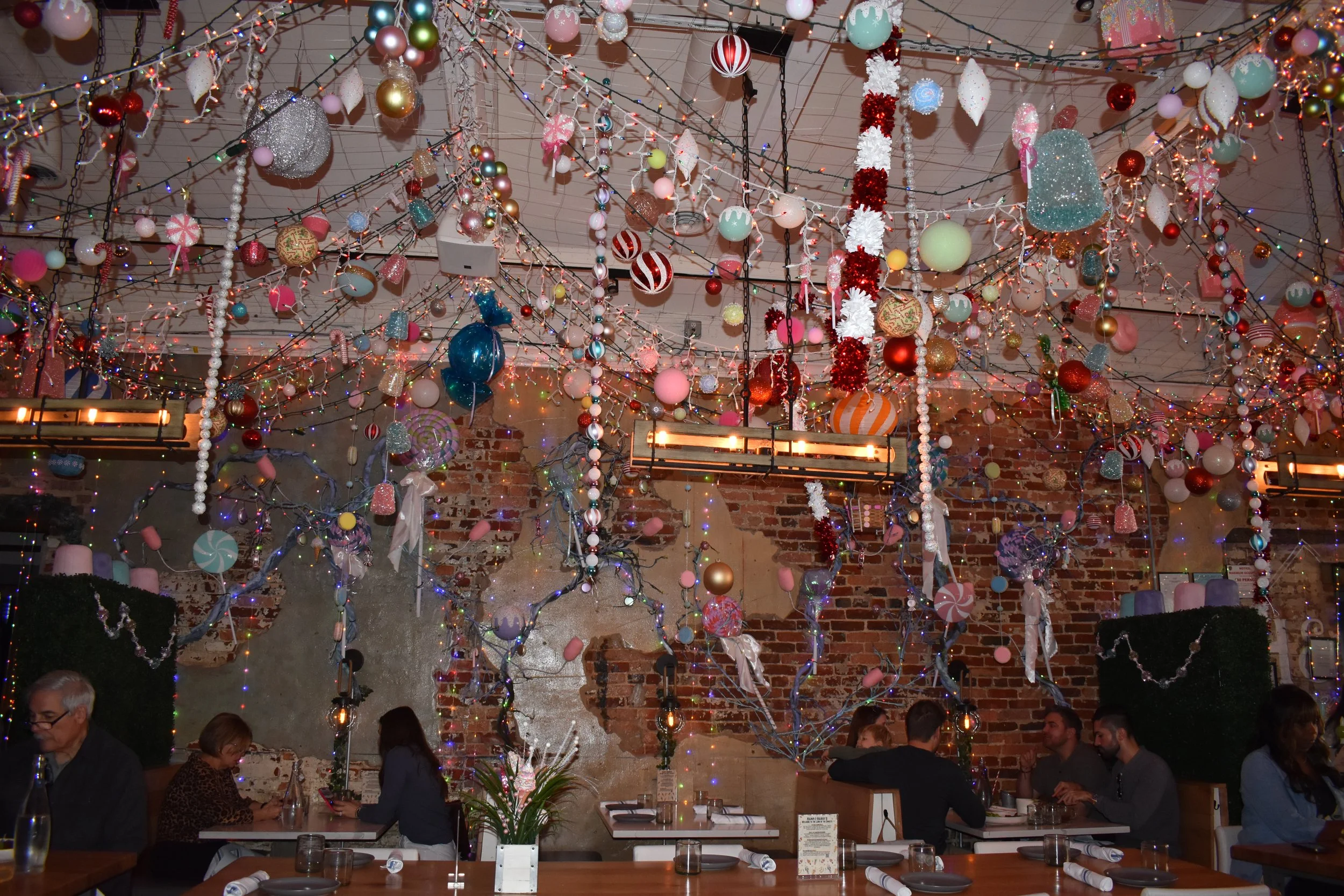 Interior of a restaurant decorated with colorful Christmas ornaments, string lights, and holiday decor hanging from the ceiling. There are people sitting at tables.