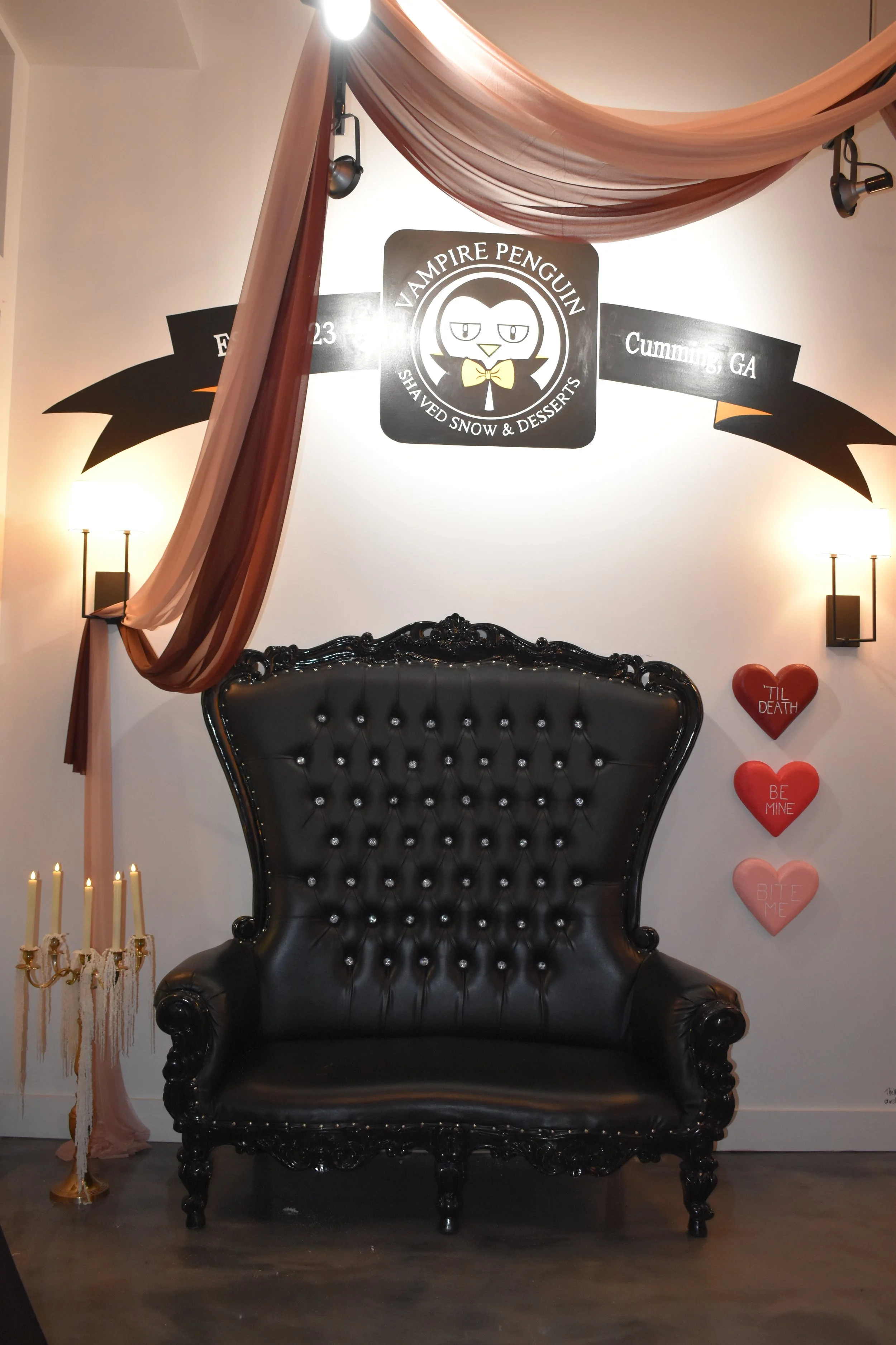 Decorative black vintage-style throne with tufted leather upholstery, surrounded by romantic Valentine’s Day hearts, candleholder, and dim lighting in a cozy, romantic setting.