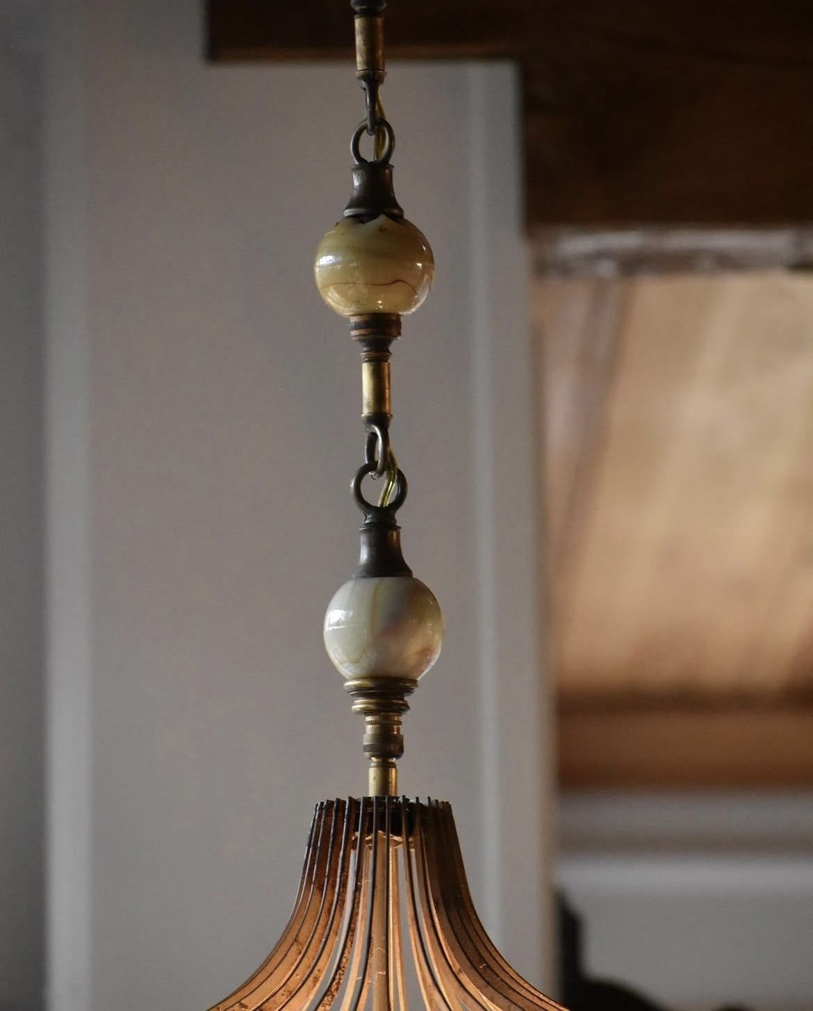 Close-up of a hanging ceiling lamp with metal slats, and decorative marble beads above the lampshade.